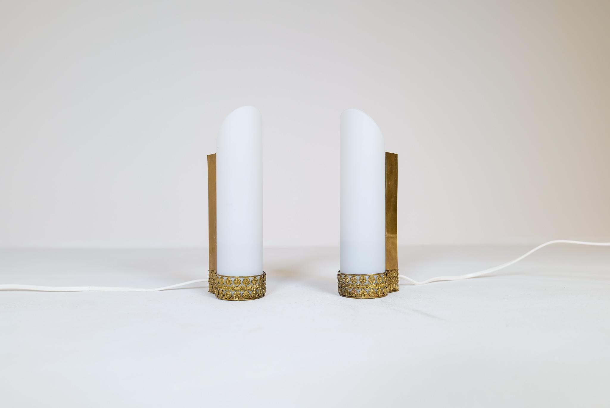 These wall mounted lamps were created in Sweden during the 1950s. They were most likely produced by ASEA. 
The ends of the base are made in brass and holds the opaline glass. Decorated bottom with relief brass pattern. 
Could be use in bathroom or
