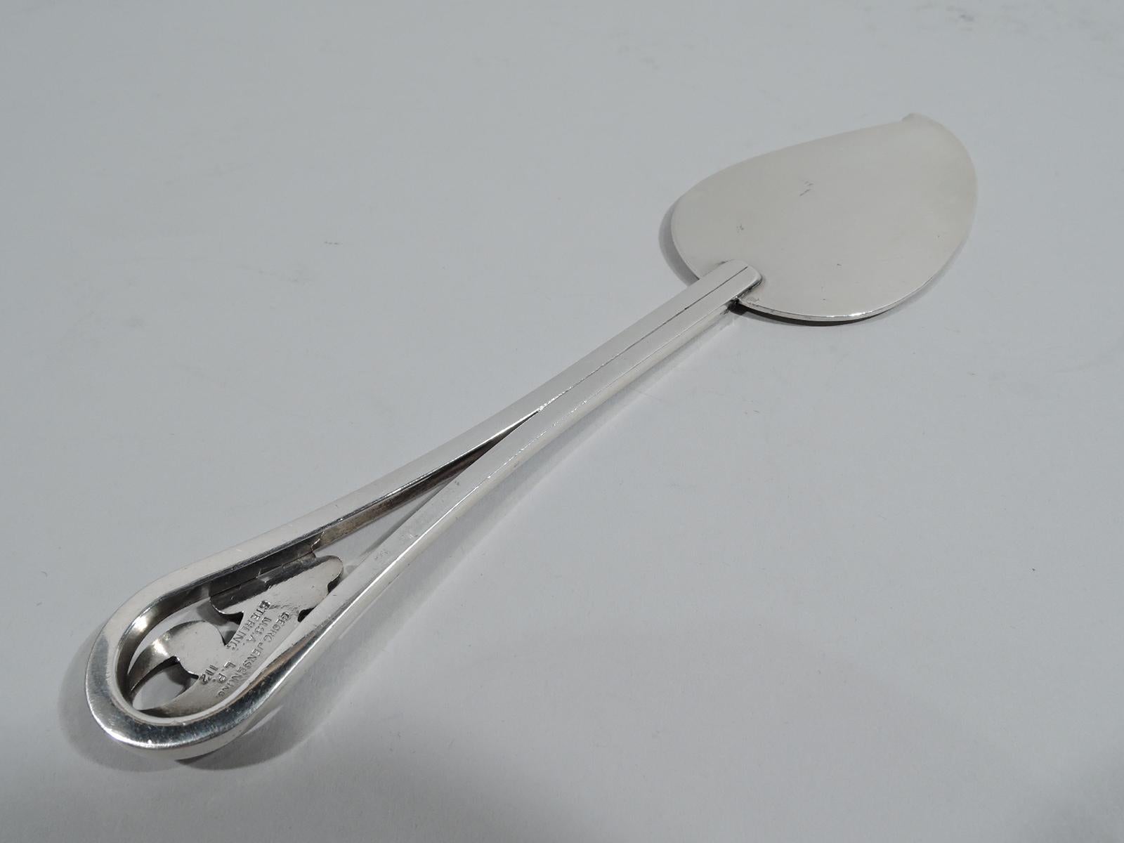 Mid-Century Modern sterling silver pastry server. Made by Alphonse La Paglia (d. 1953) for Georg Jensen USA. Flat and joined handle and open oval terminal inset with scrolled leaf and flower. Handle base has hatched lines. Curve shaped blade. A