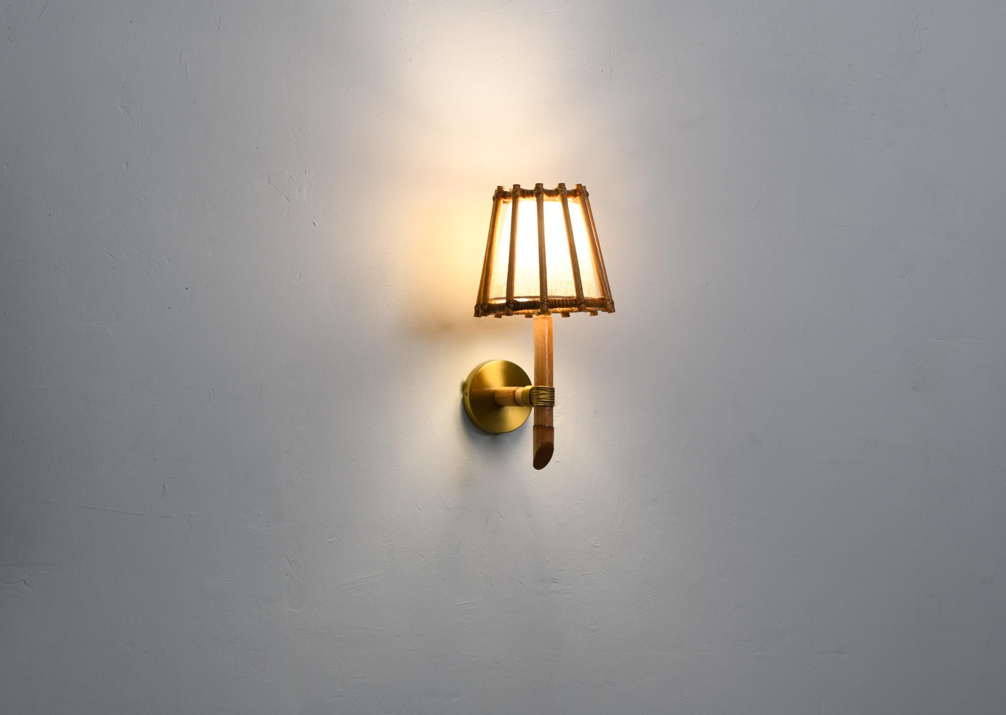 Hecho a mano con esmero utilizando ratán natural, nuestro aplique de estilo moderno de mediados de siglo aporta un toque de encanto artesanal a cualquier espacio. El poste de ratán, acentuado con oro, añade un toque único y elegante. Eleva la