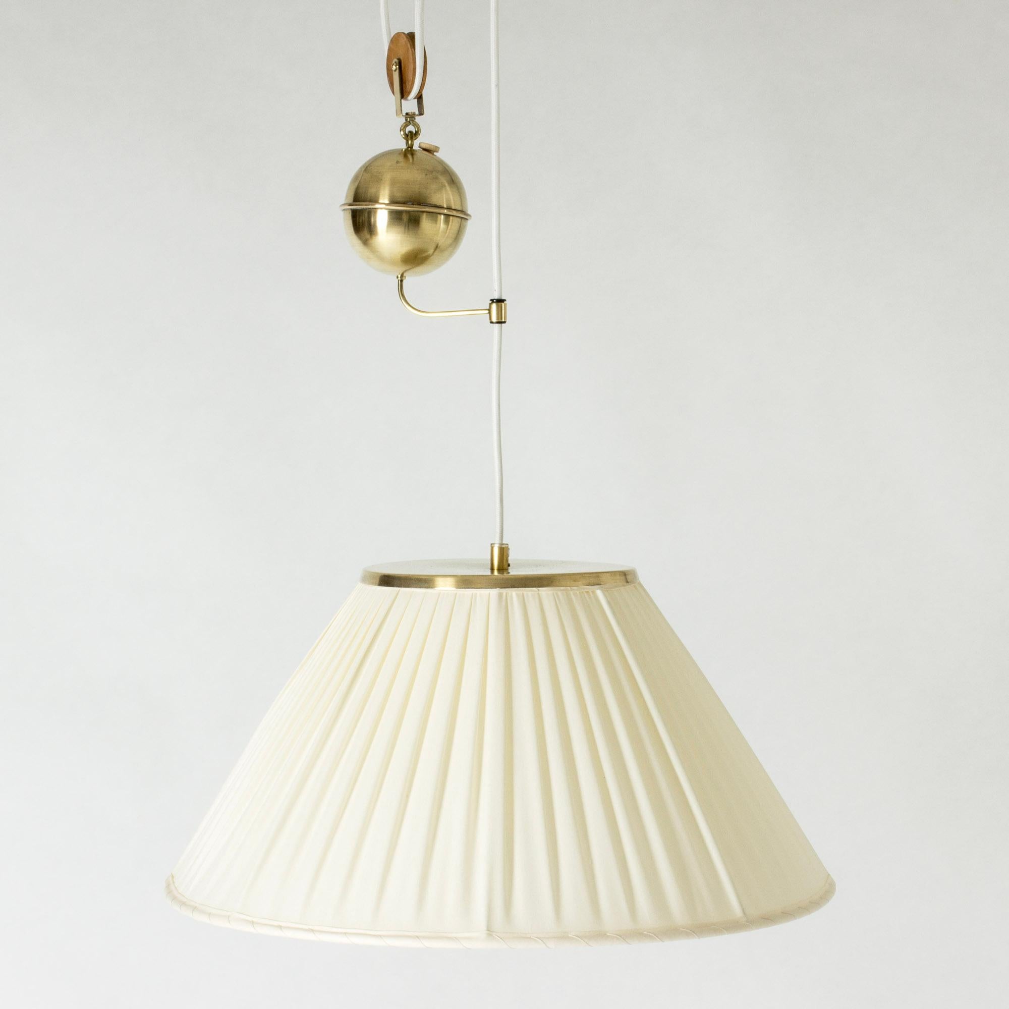 Beautiful brass pendant light by Josef Frank, in an elegant, voluminous design. Shade made from pleated fabric. A decorative brass sphere can be slid up and down on the chord to adjust its length. The elegant mechanism is a great part of the