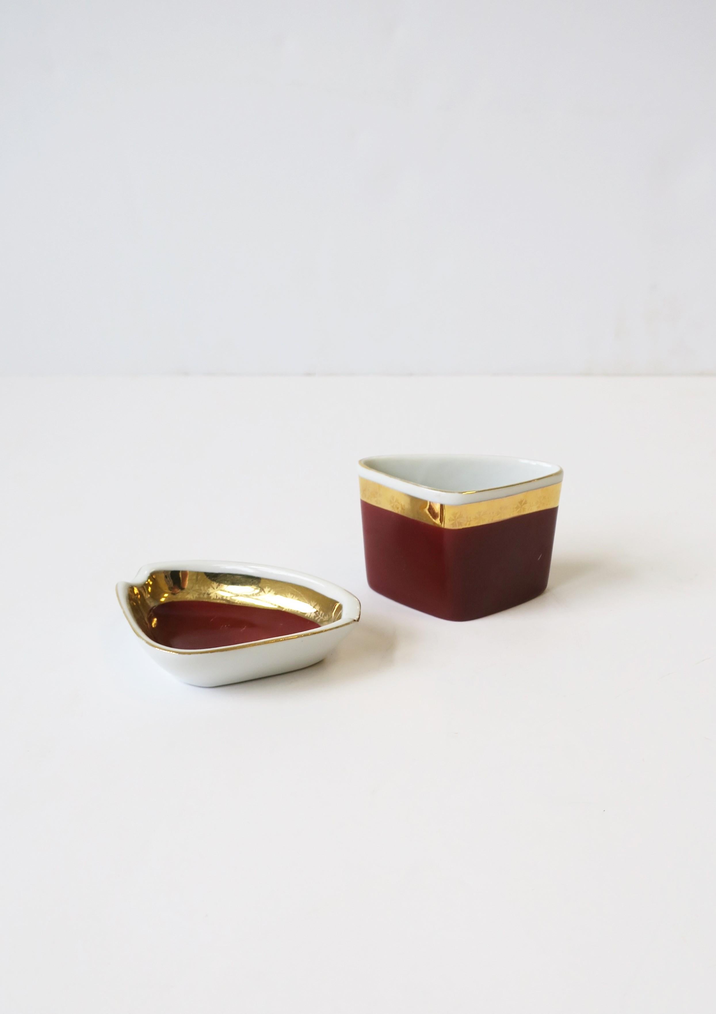 A Hungarian porcelain ashtray and loose cigarette vessel holder set, Mid-Century Modern, circa early to mid-20th century, Hungary by Hollohaza. Set has a triangular shape with gold and red burgundy hues. A great set for a home bar, library, etc.