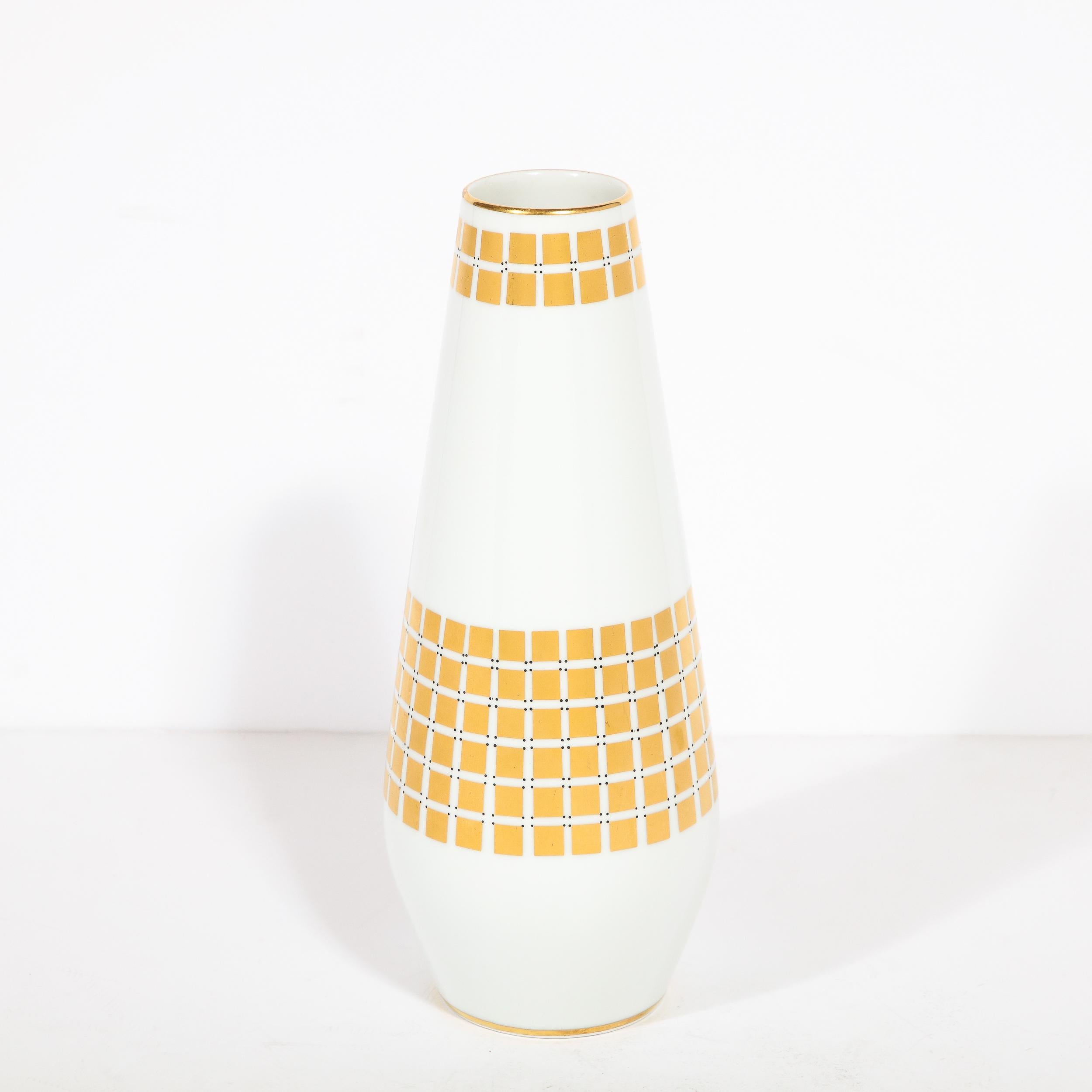 
This elegant Mid Century Modern porcelain vase was realized by the esteemed maker Tirschenheut in Germany circa 1960. It features a cylindrical body in white porcelain that flares subtly from its circular base before tapering to a round mouth. The