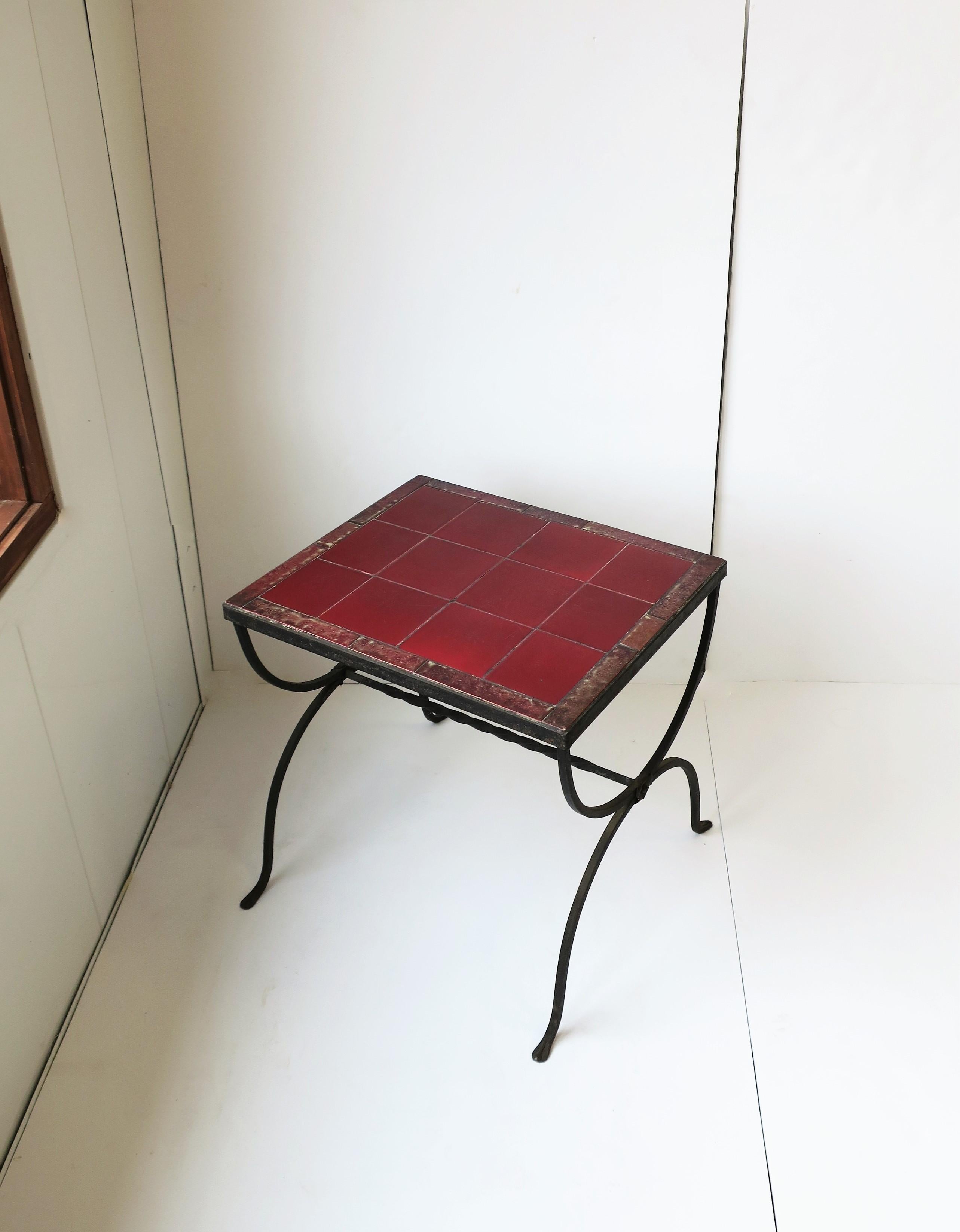 A substantial rectangular red burgundy ceramic tile top and iron end, side, or drinks table, in the Regency/Spanish Revival style, circa mid-20th century. Table has a black iron metal frame with arched design and pad feet. Top includes twelve square