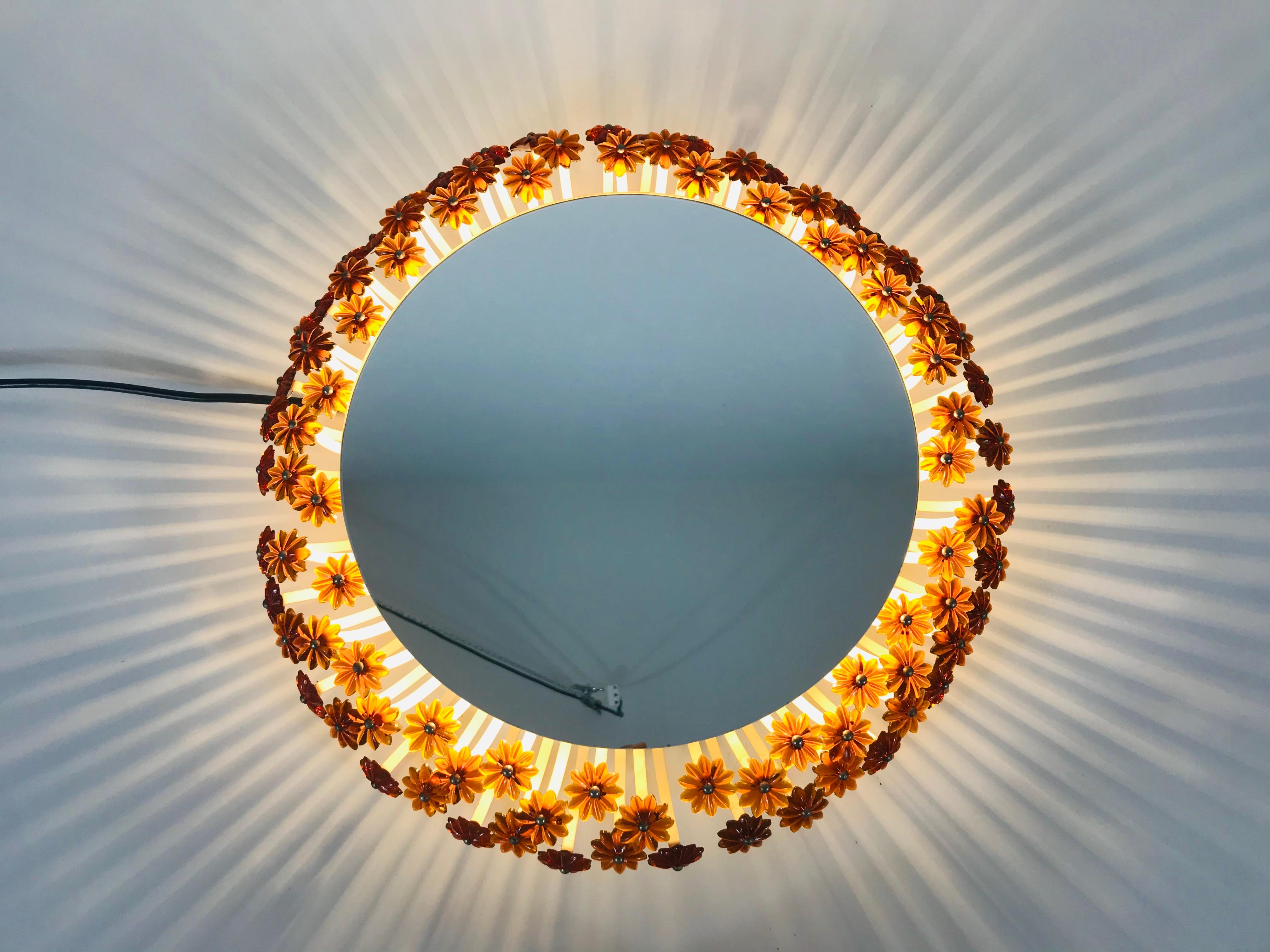 Un miroir mural éclairé des années 1960 fabriqué en Autriche. Il a été conçu par Emil Stejnar pour Rupert Nikoll. Le miroir a un design rond avec de belles fleurs en acrylique orange. Il y a une douille E27 à l'intérieur du cadre. Le miroir est en