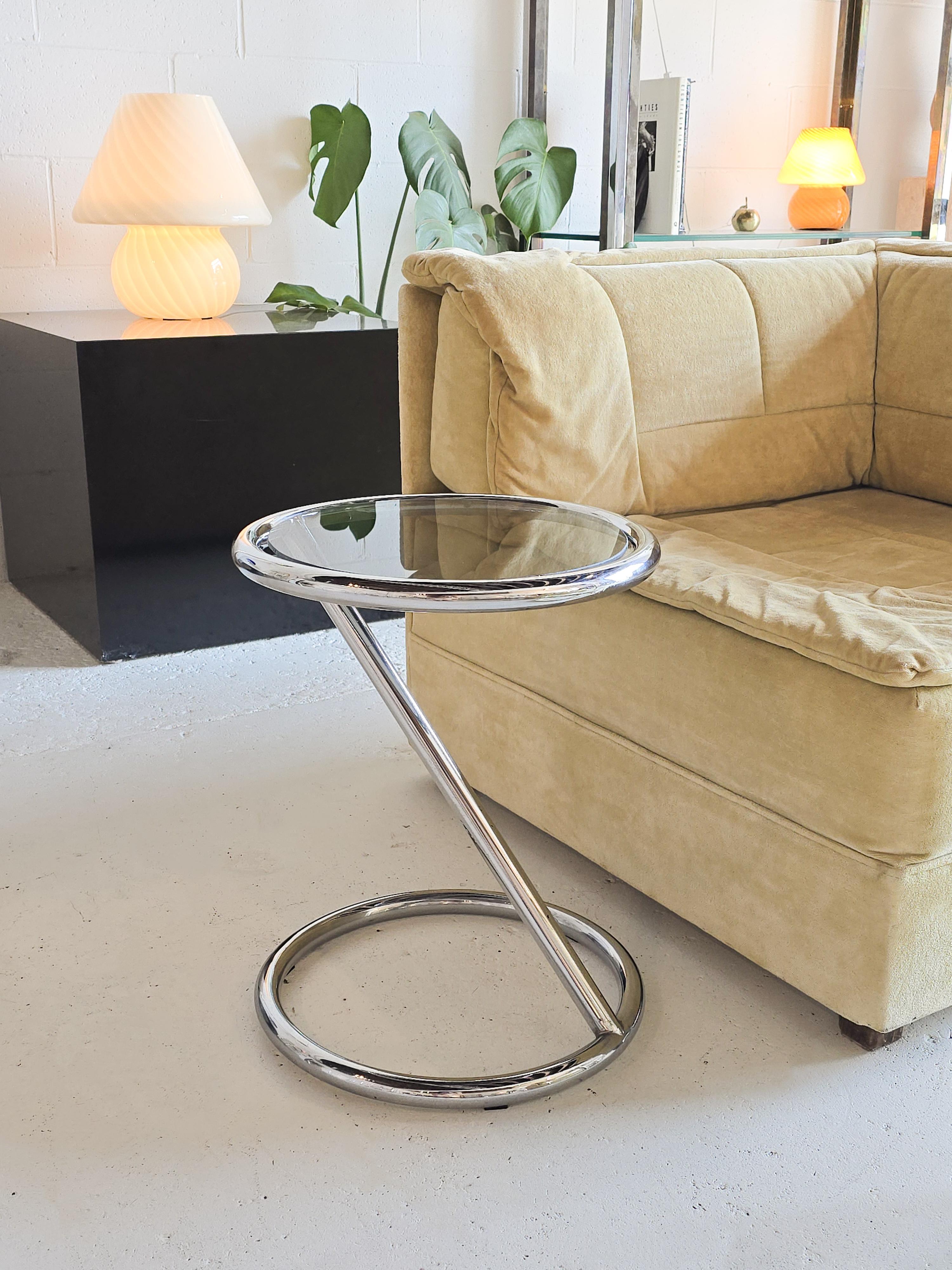 Sculptural tubular chrome side table featuring tinted glass top. The base of this side table is a tubular chrome. It has a sculptural shape. It features a glass top that is tinted dark glass. 
In good vintage condition with some signs of wear.