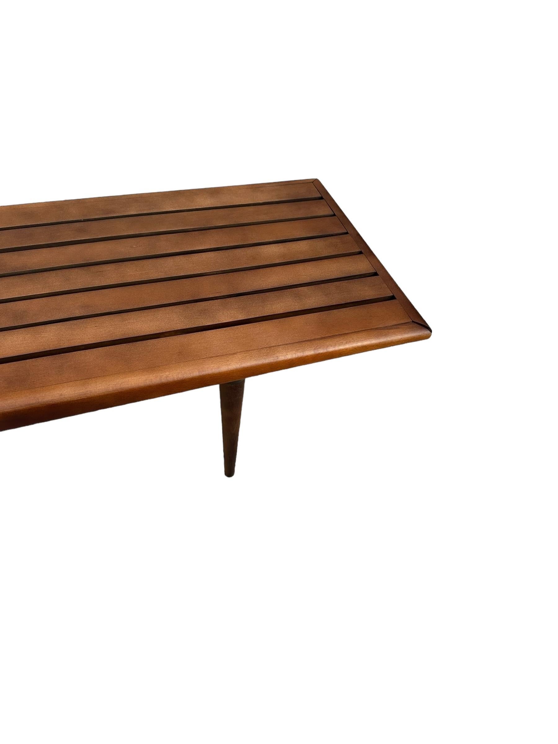 Beautiful solid wood slat bench in classic Midcentury Modern style. Perfect to use as a coffee table as well. Tabletop and sides and legs have been completely stripped and sanded, with  refinishing medium walnut tone. Sealed with satin lacquer. Legs