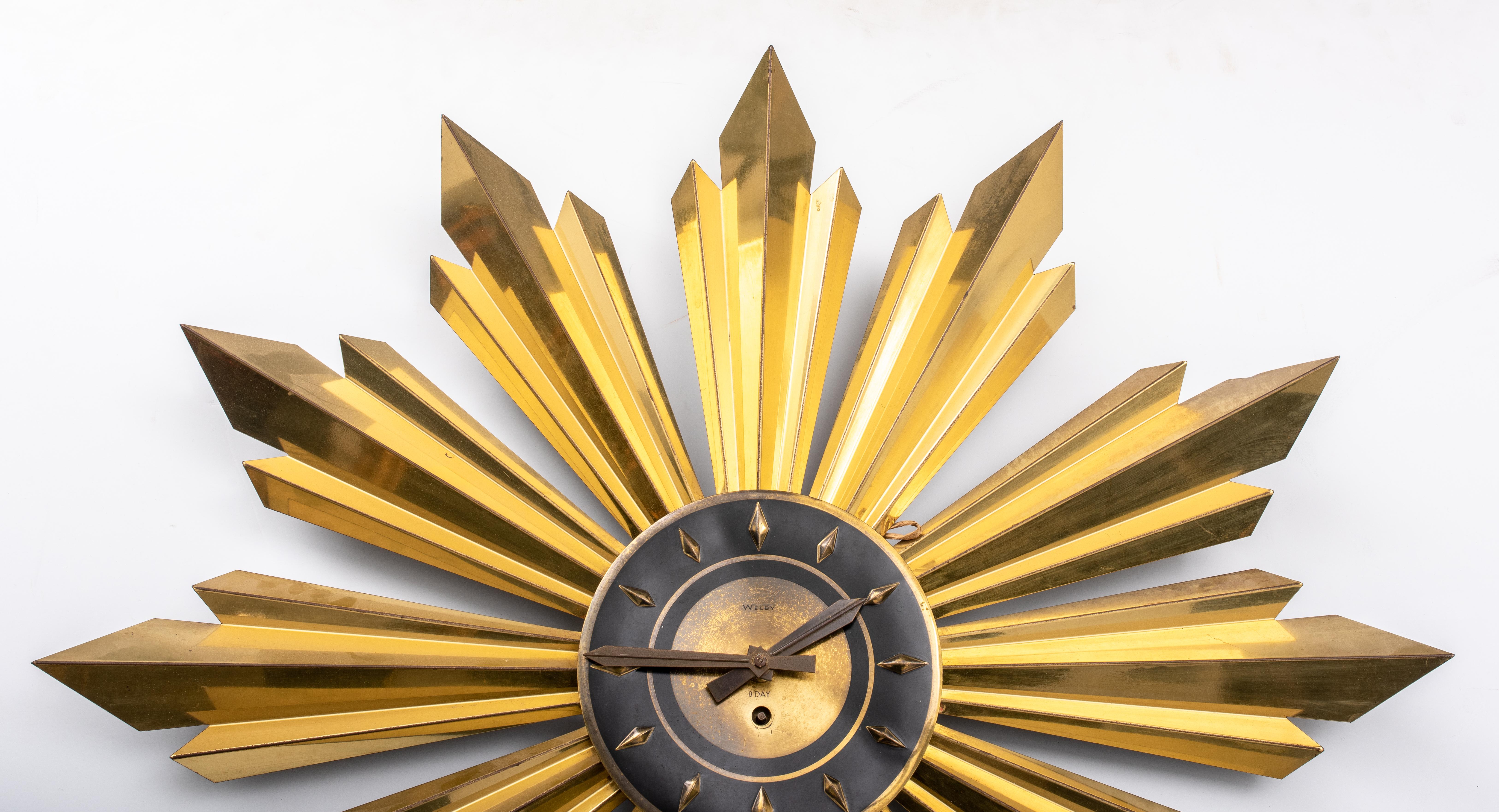 Mid-Century Modern sunburst wall clock in patinated and burnished brass, with 12 multi-faceted rays in splendor, the clock with blind dial. 

Measures: 27