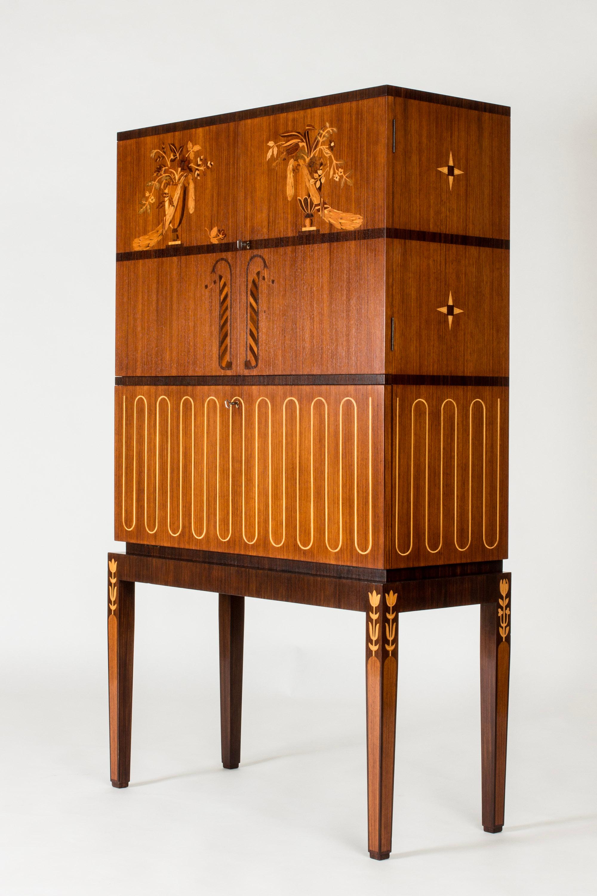 Einzigartiger Barschrank von Axel Einar Hjorth, in einem auffallend dekorativen Design mit eleganten Details. Gefertigt aus Mahagoni mit floralen Intarsien aus Birke und Palisanderholz. Beleuchtung innen. Spiegel an der Rückwand, ausklappbares Regal