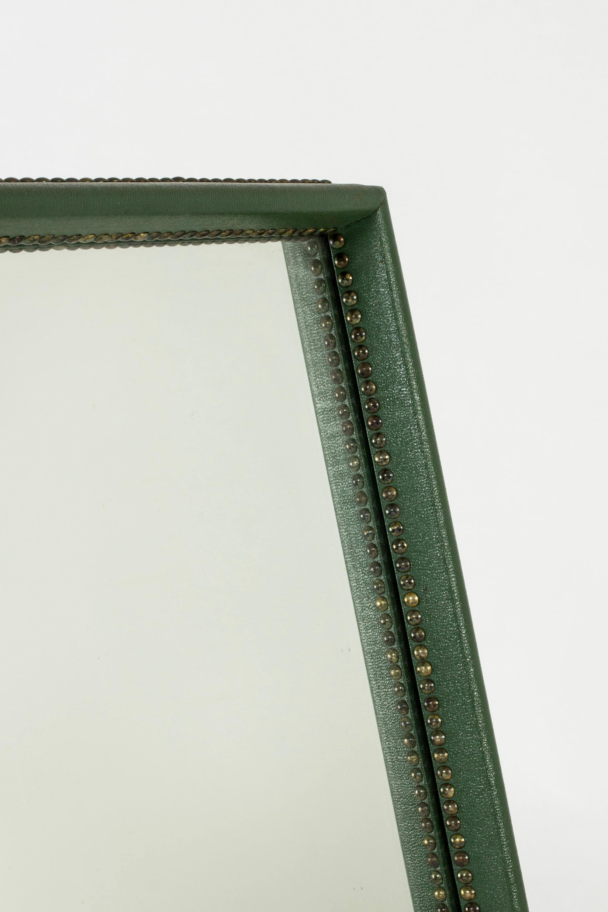 Elegant wall mirror by Otto Schulz. Frame dressed in dark green faux leather, decorated around the inner and outer edges with numerous brass nails.