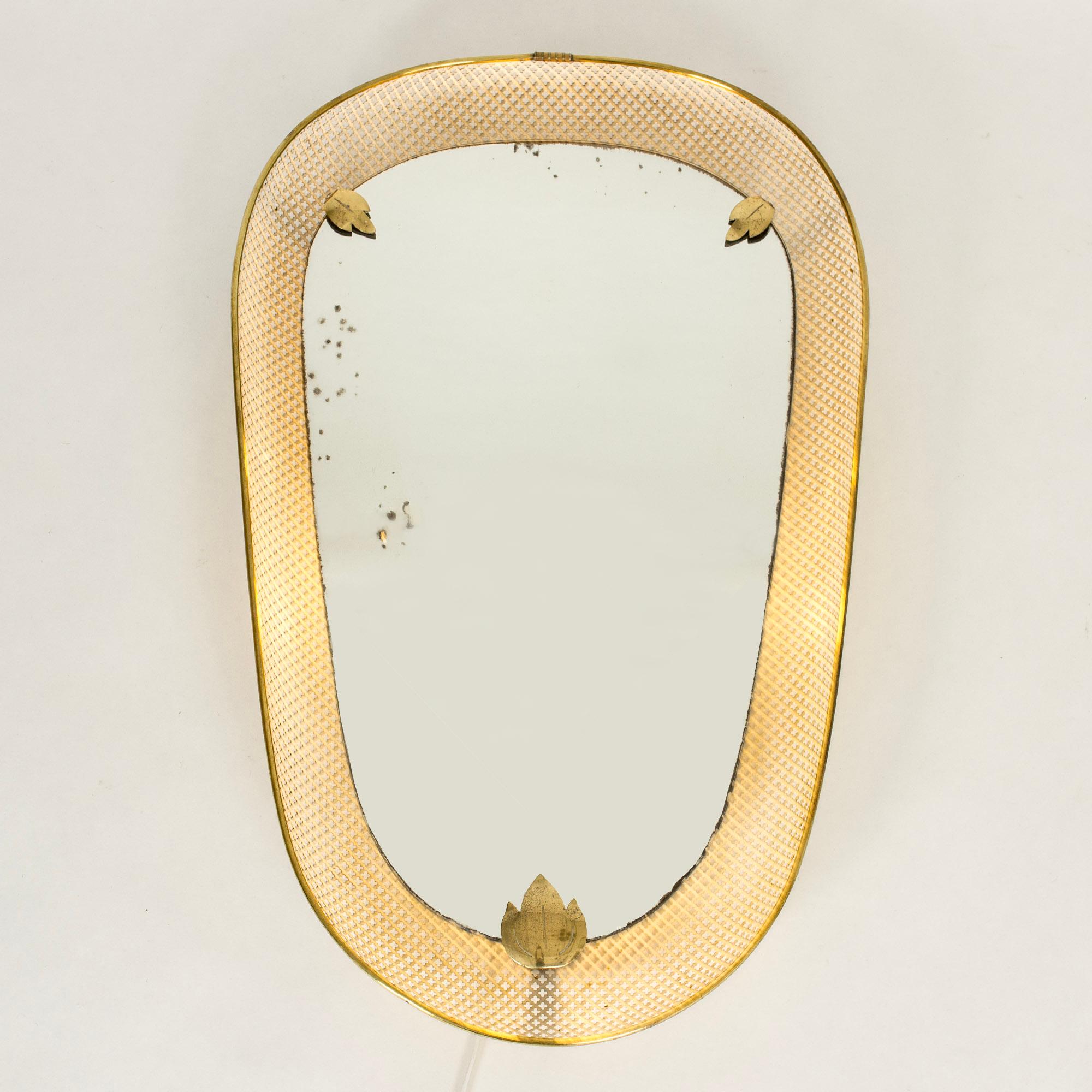 Elegant Swedish Modern wall mirror, lit from behind so that light glows around the edge of the mirror glass. Made from white lacquered metal with cutout clover pattern, brass rim and decorative leaves. Original glass with some small losses.