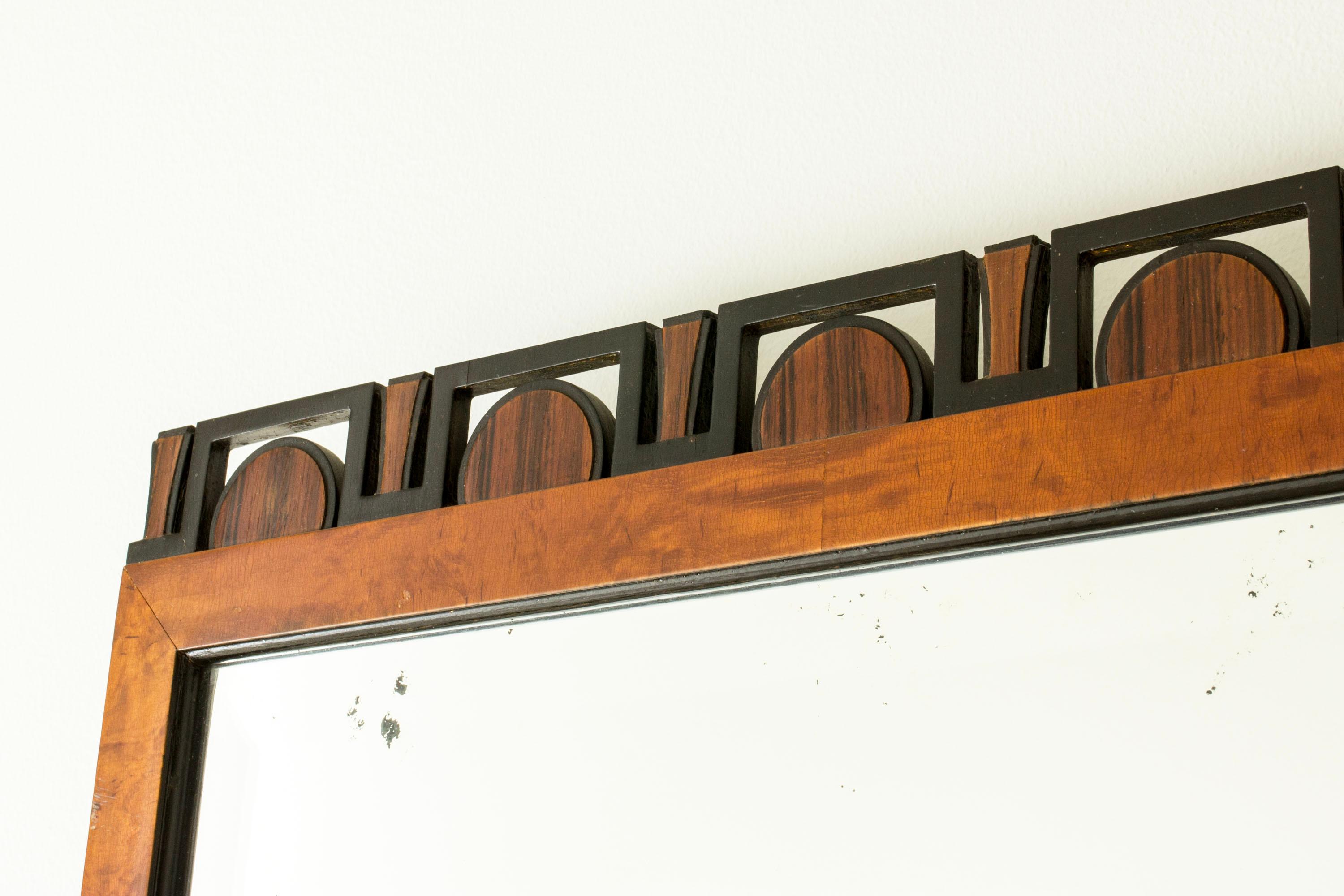 Eleganter schwedisch-moderner Wandspiegel, mit einem Holzrahmen. Grafisches Dekor aus Halbkreisen und Quadraten in schwarz lackiertem Holz an der Oberseite des Rahmens.