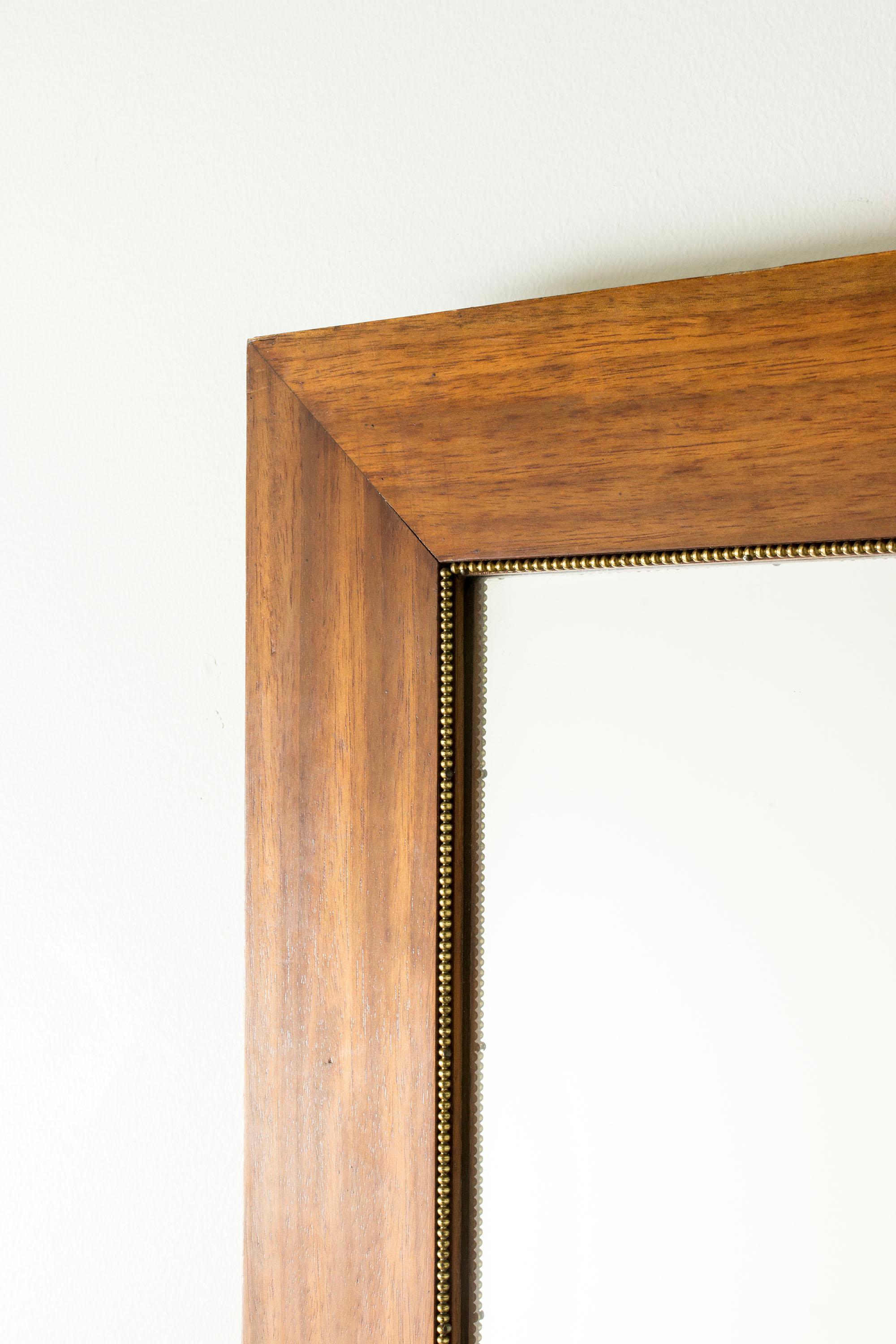 Elegant miroir mural suédois moderne, avec un large cadre lisse en acajou. Joli décor subtil d'une ligne de perles en laiton sur le bord intérieur du cadre.