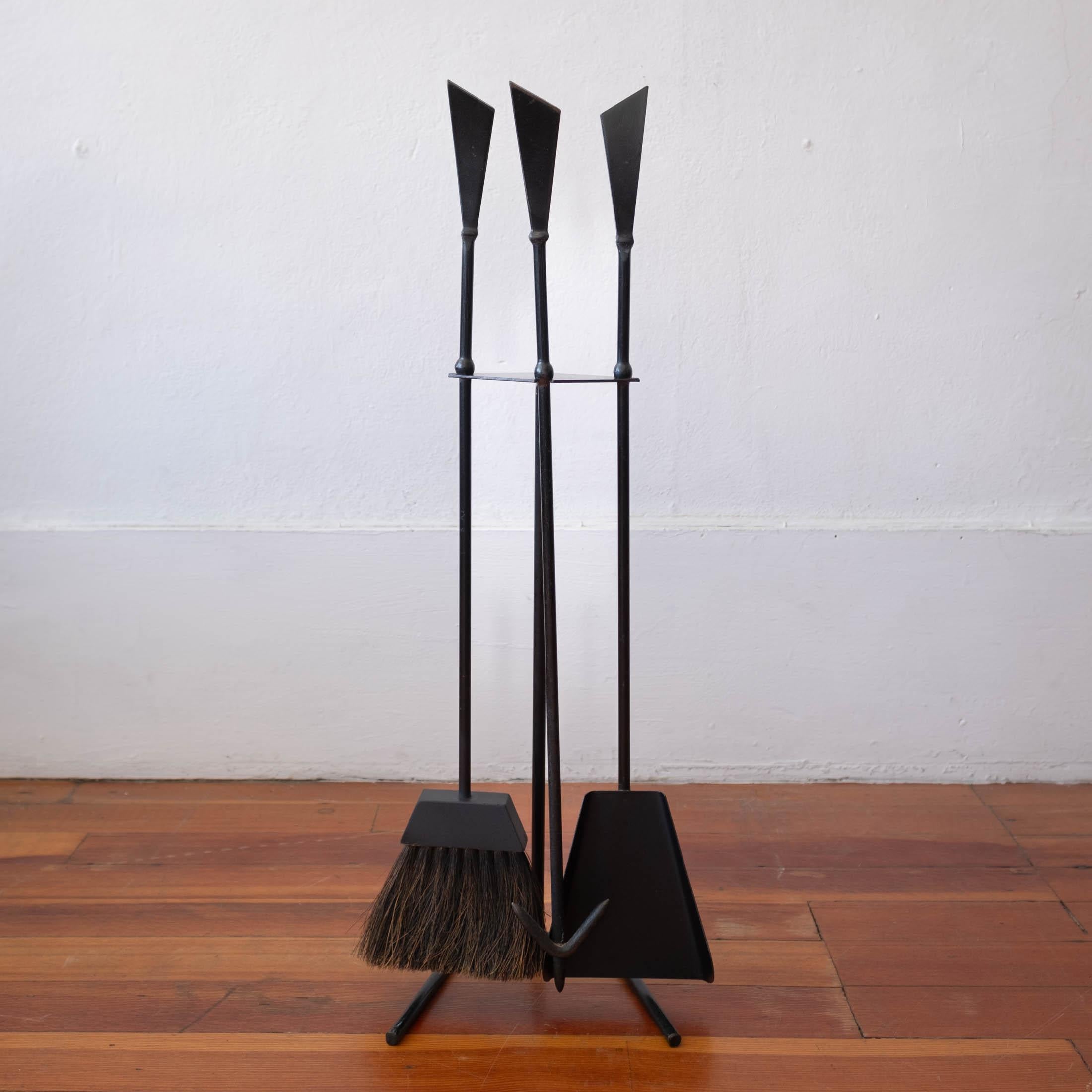 A fantastic modernist iron fire tool set. Includes a poker, brush and shovel on a solid iron stand. USA, 1950s