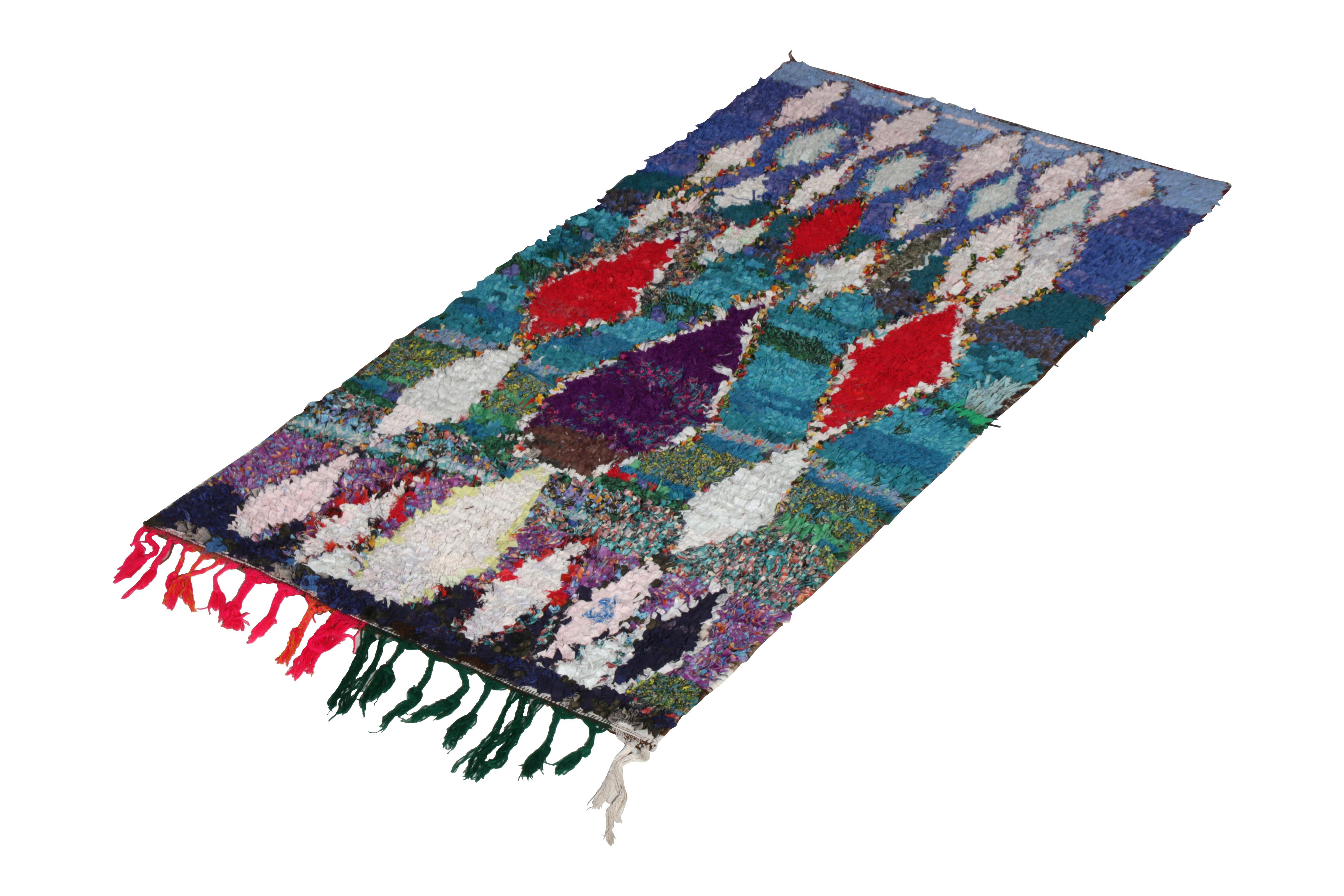 A colorful addition to the home, this vintage Moroccan wool rug was handmade circa 1950-1960, idealizing the Berber tribal rug style. This particular edition of the mid-century vintage Moroccan rug relies on blue, red, and purple fabric creating