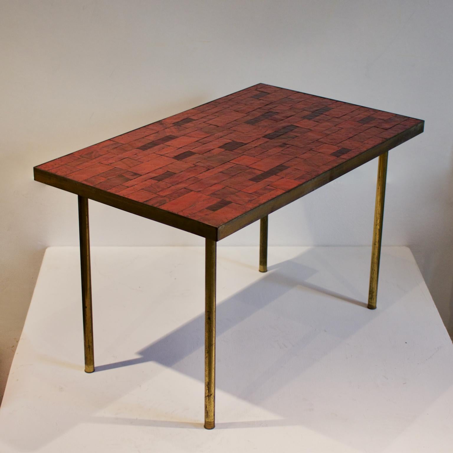 A mosaic side table in warm red tones, by Berthold Müller, Germany, mid-20th century.

The table is covered in rectangular stone mosaic tiles on wood, with a bronze or brass surround. The top sits on brass legs, each screwed into the wood. This