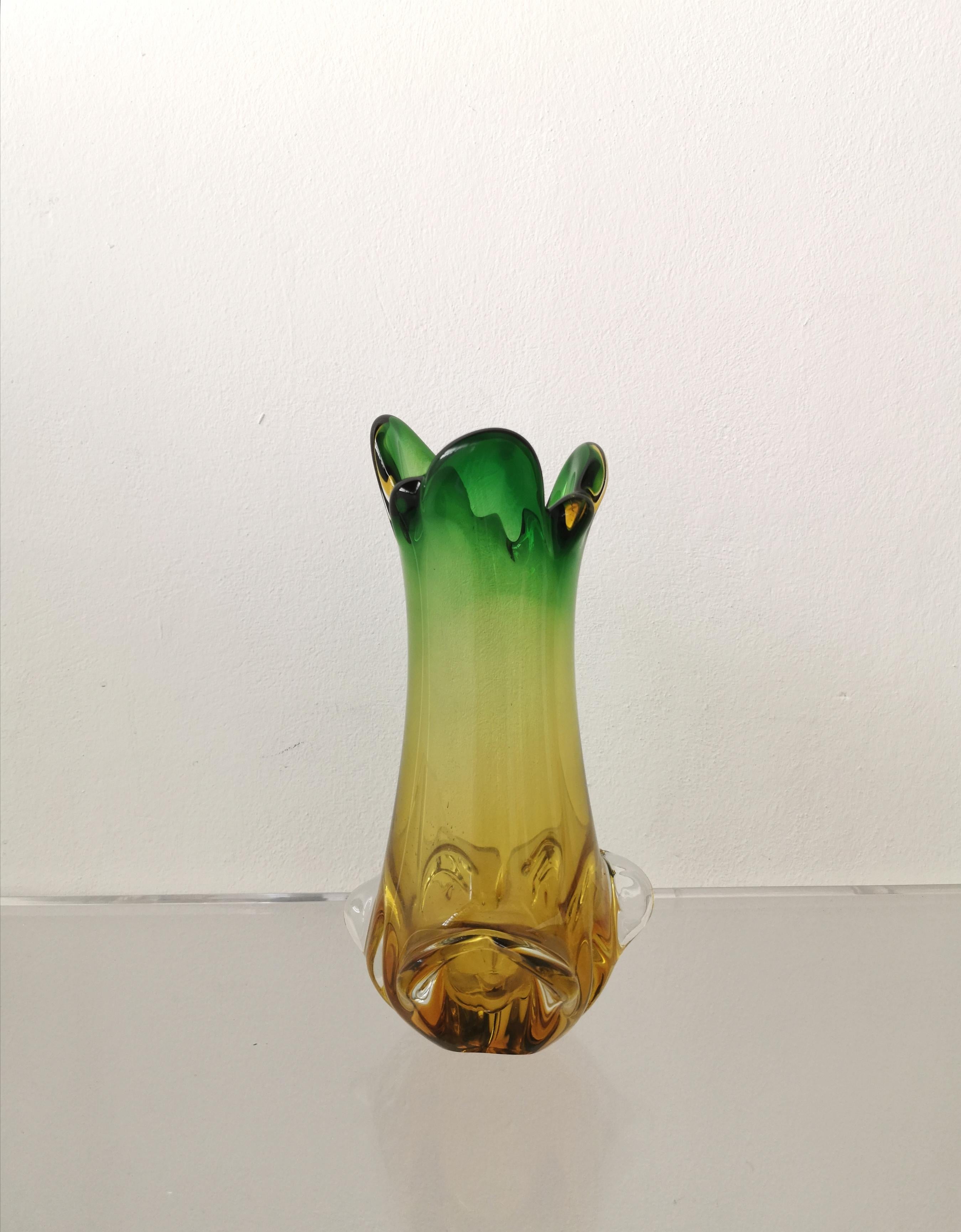 Vase produced in Italy in the 70s by the Italian company De Majo. The vase is in submerged Murano glass with an informal body with relief decorations in the lower part and a trefoil mouth with rounded corners in green and amber tones.