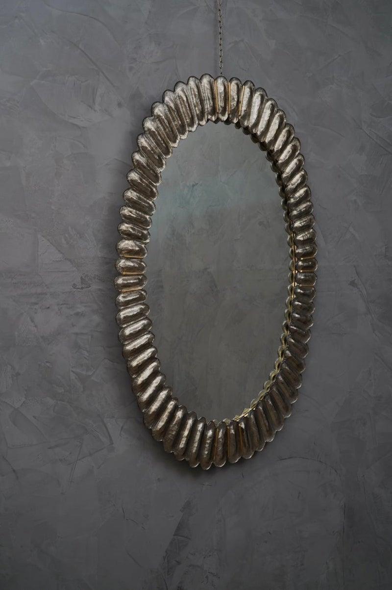 Wunderschöner Spiegel aus silberfarbenem Murano-Glas, Venedig. Ein Spiegel, der allein Ihr Zuhause einrichtet.

Der Spiegel hat eine Rückwand aus Holz, auf der vier Murano-Glasscheiben montiert sind, die wie auf dem Foto ein Oval bilden. Der