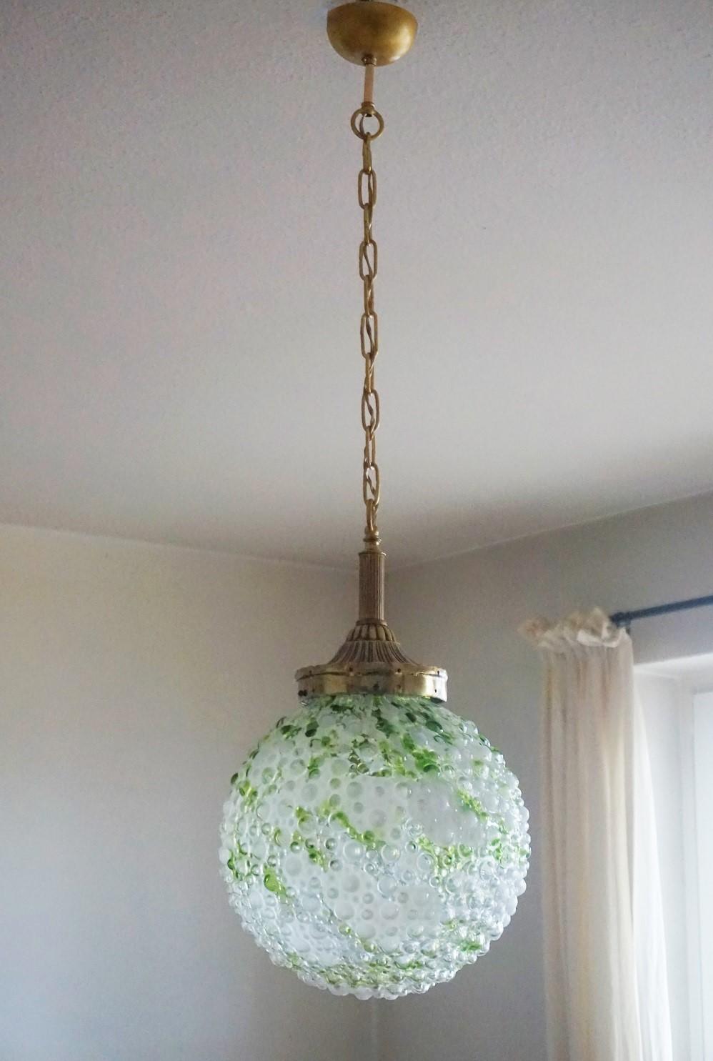 A Murano white and green glass pendant with solid brass mounts and thick and heavy glass ball, Italy, 1950s. 
One E27 light socket for a large sized bulb up to 100Watt.
This wonderful light fixture is in very good condition, aged patina to brass, no