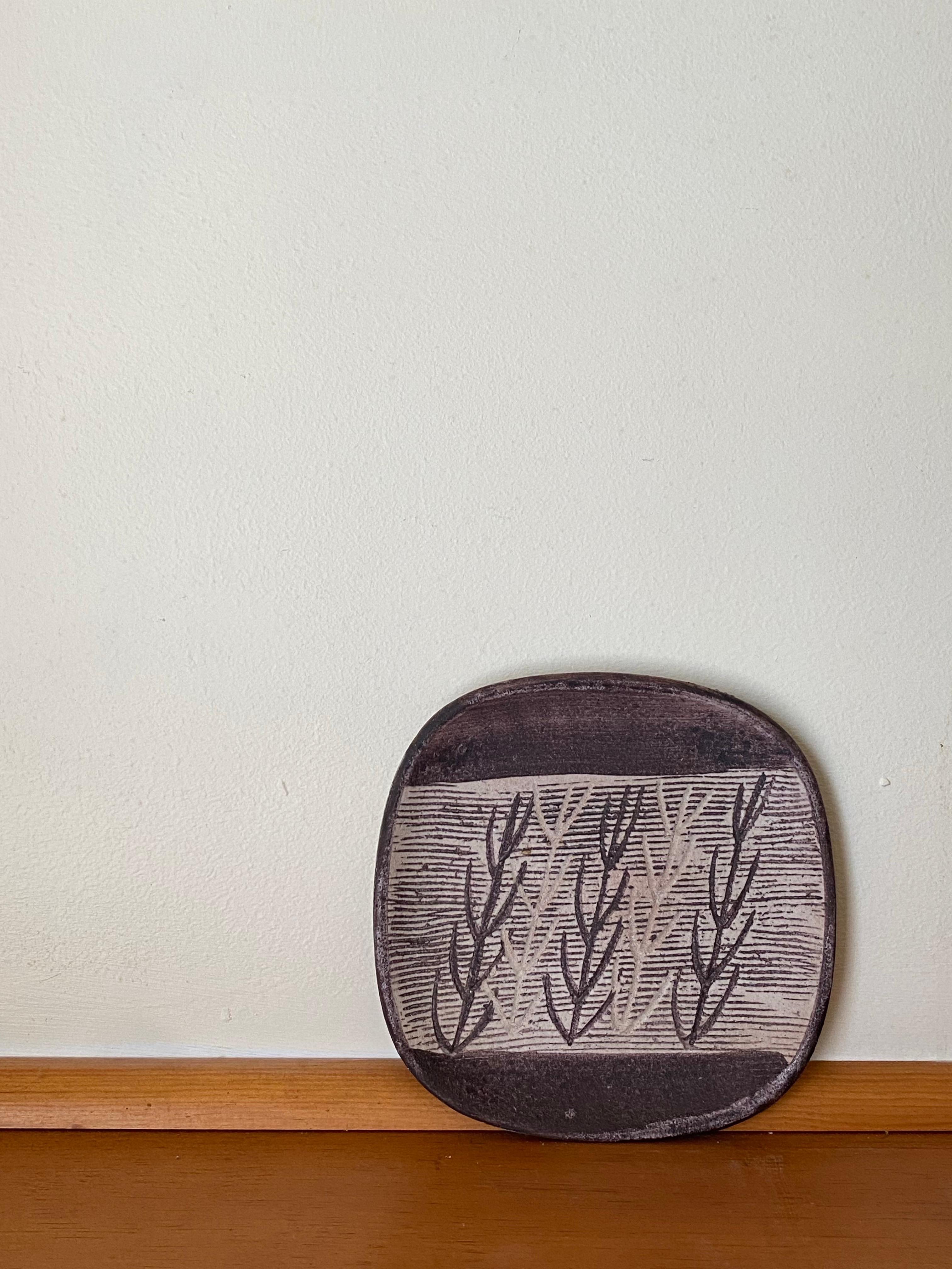 A late 1940s stoneware plate by Nancy Wickham Boyd featuring a dynamic design motif of bare twigs. The curved organic shape of the plate is a nice compliment to the more severe carving of the twigs. Like quite a few well-known NYC potters Nancy got