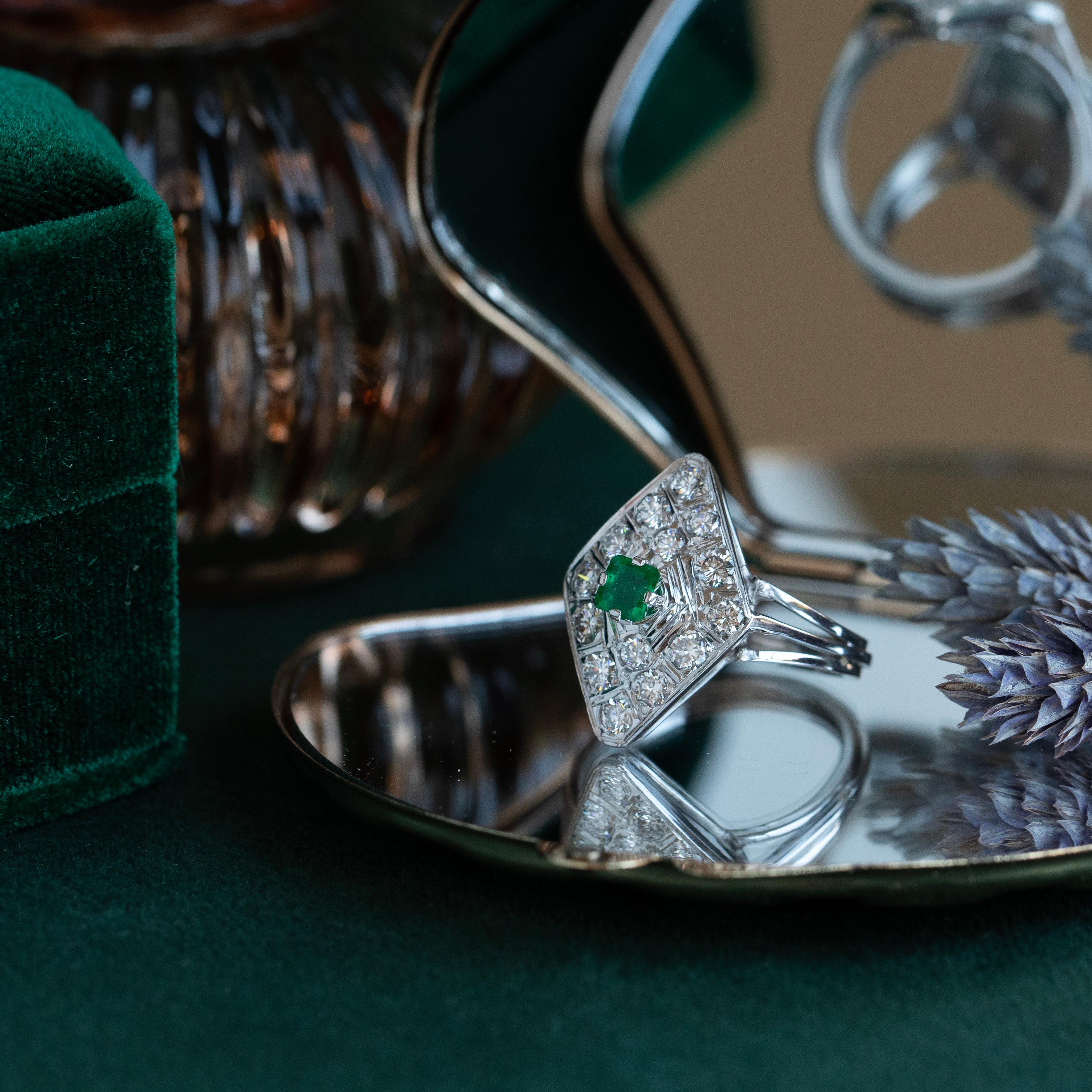 A rich green emerald perches atop more than one carat of brilliant, fiery diamonds in this delightfully luxurious cocktail ring. The lozenge shape and full-finger coverage is reminiscent of the glamour of mid-century cocktail parties and the freer