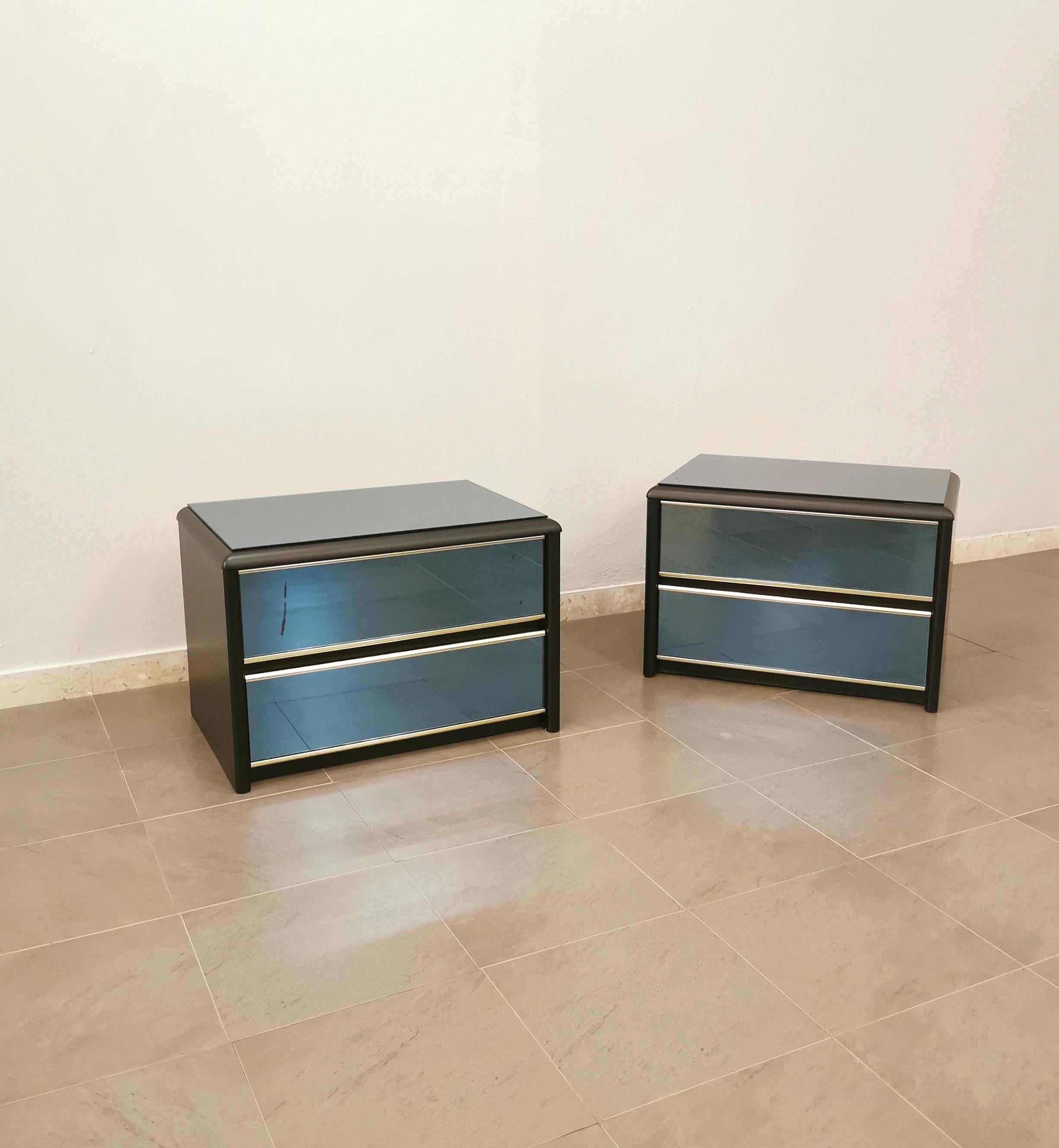 Set of 2 bedside tables by an unknown designer produced in Italy in the 70s. This elegant set has a matte effect black wood structure and rounded edges with cobalt-colored mirrored glass top and drawers and golden aluminum finishes.