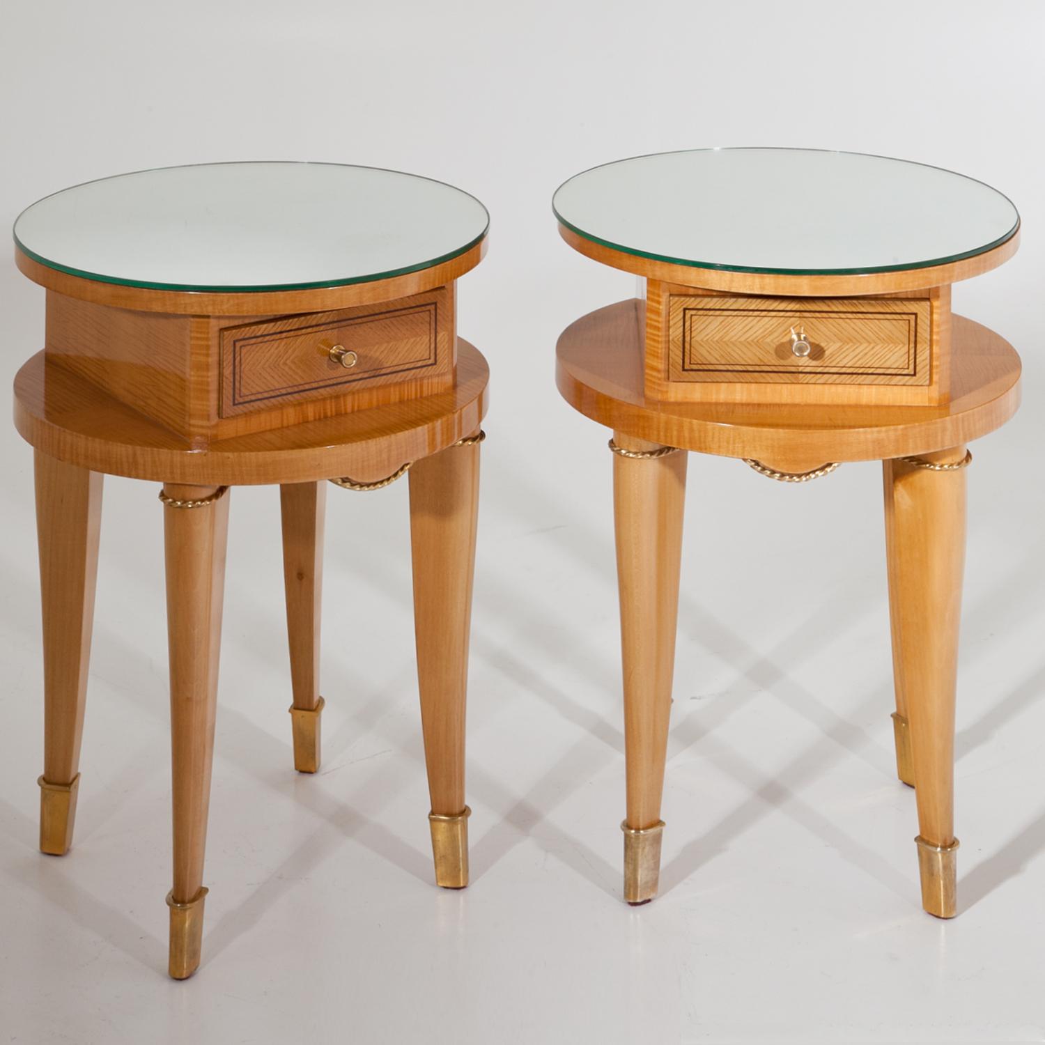 Pair of side tables or nightstands on tall tapered legs with brass sabots and twisted rings. The round tabletop is covered with a mirror pane, underneath is one small drawer. Unrestored condition.