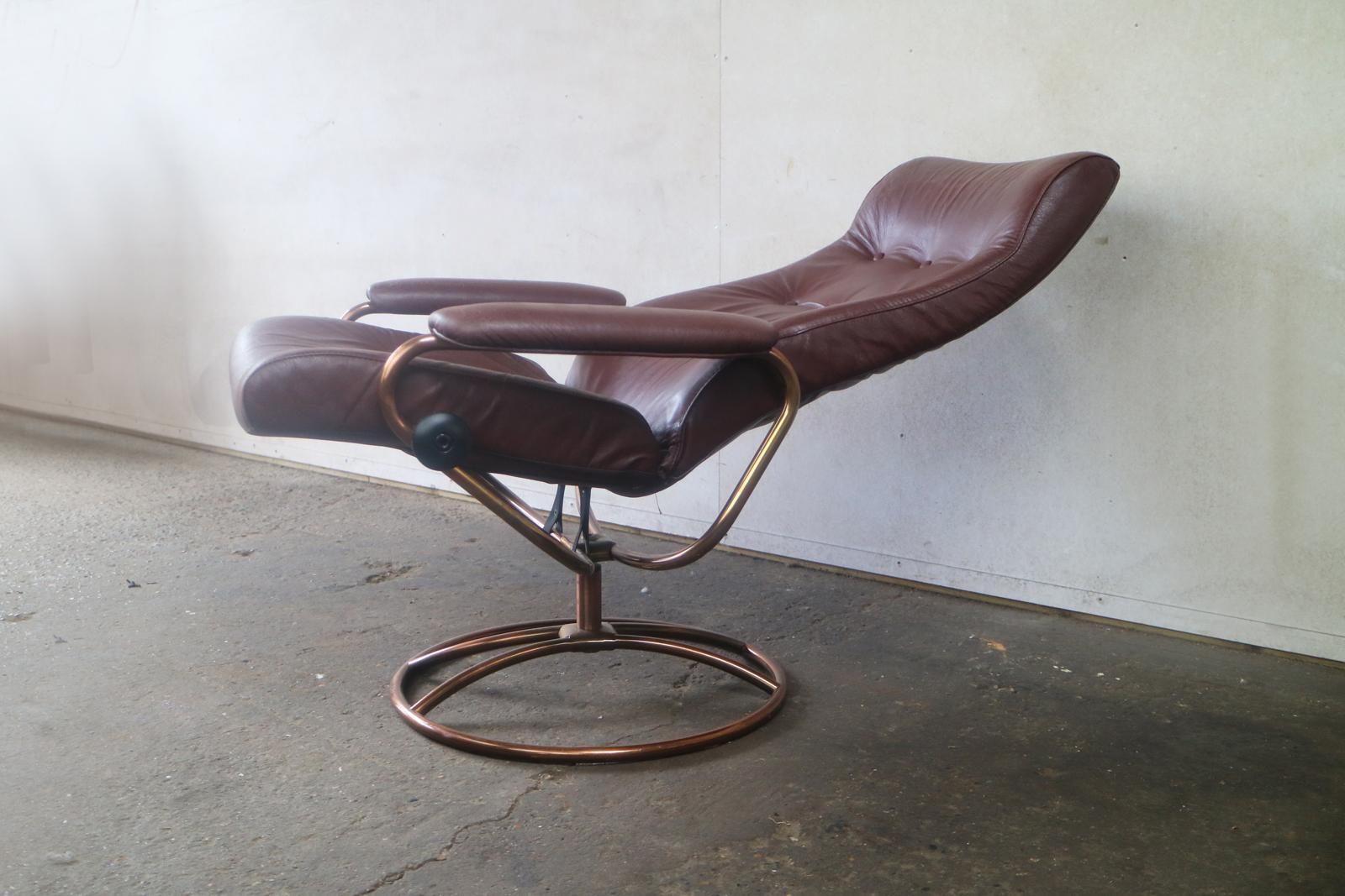 Mid-Century Modern Ekornes Stressless reclining lounge chair and ottoman featuring a brass frame and swivel base with the original maroon leather upholstery. 

Stressless recliners were made by Ekornes and introduced in 1971 in Norway and are the