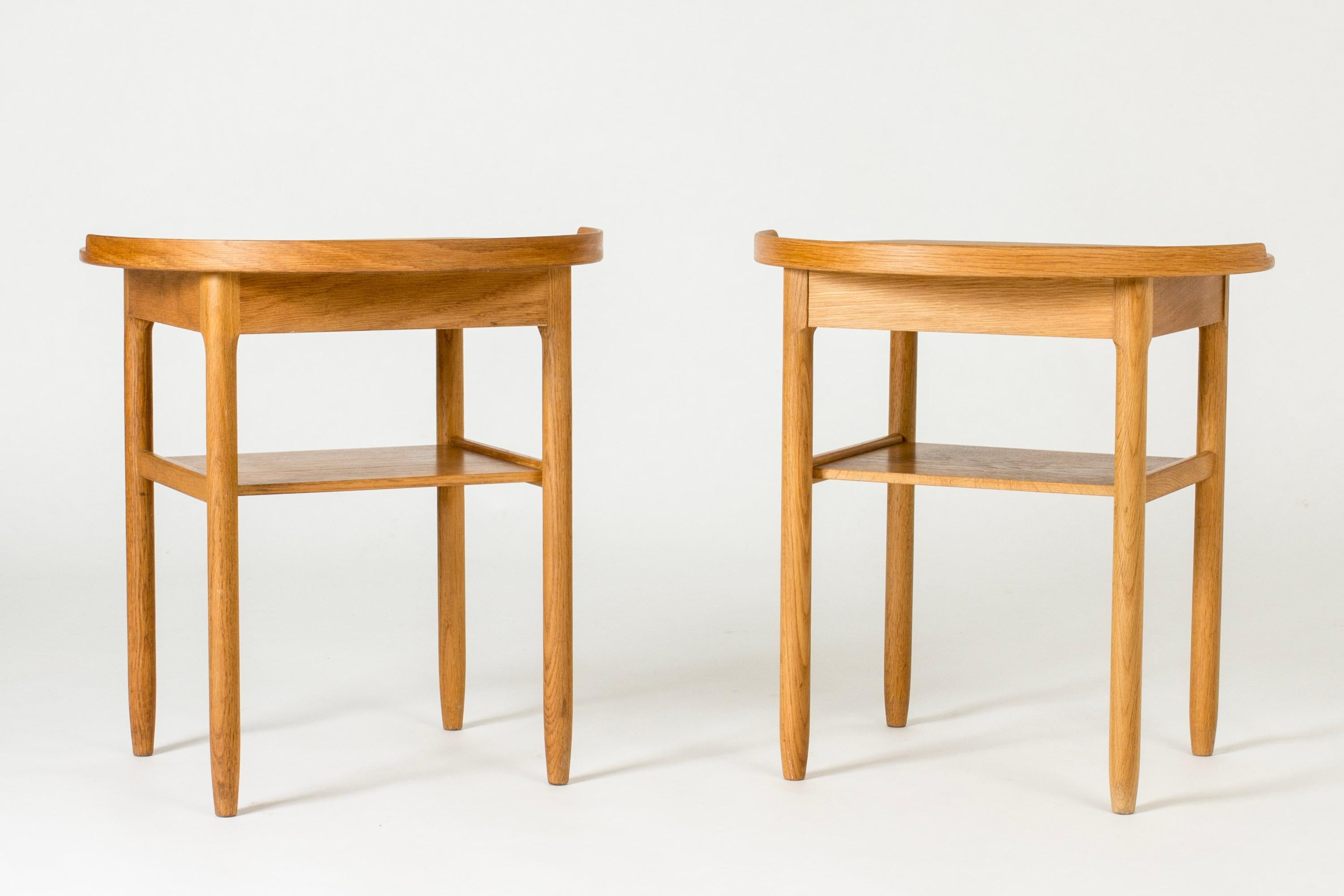 Pair of neat bedside tables by Sven Engström and Gunnar Myrstrand, made from oak. Rounded design with sculpted drawer handles and a rim around half the table tops.