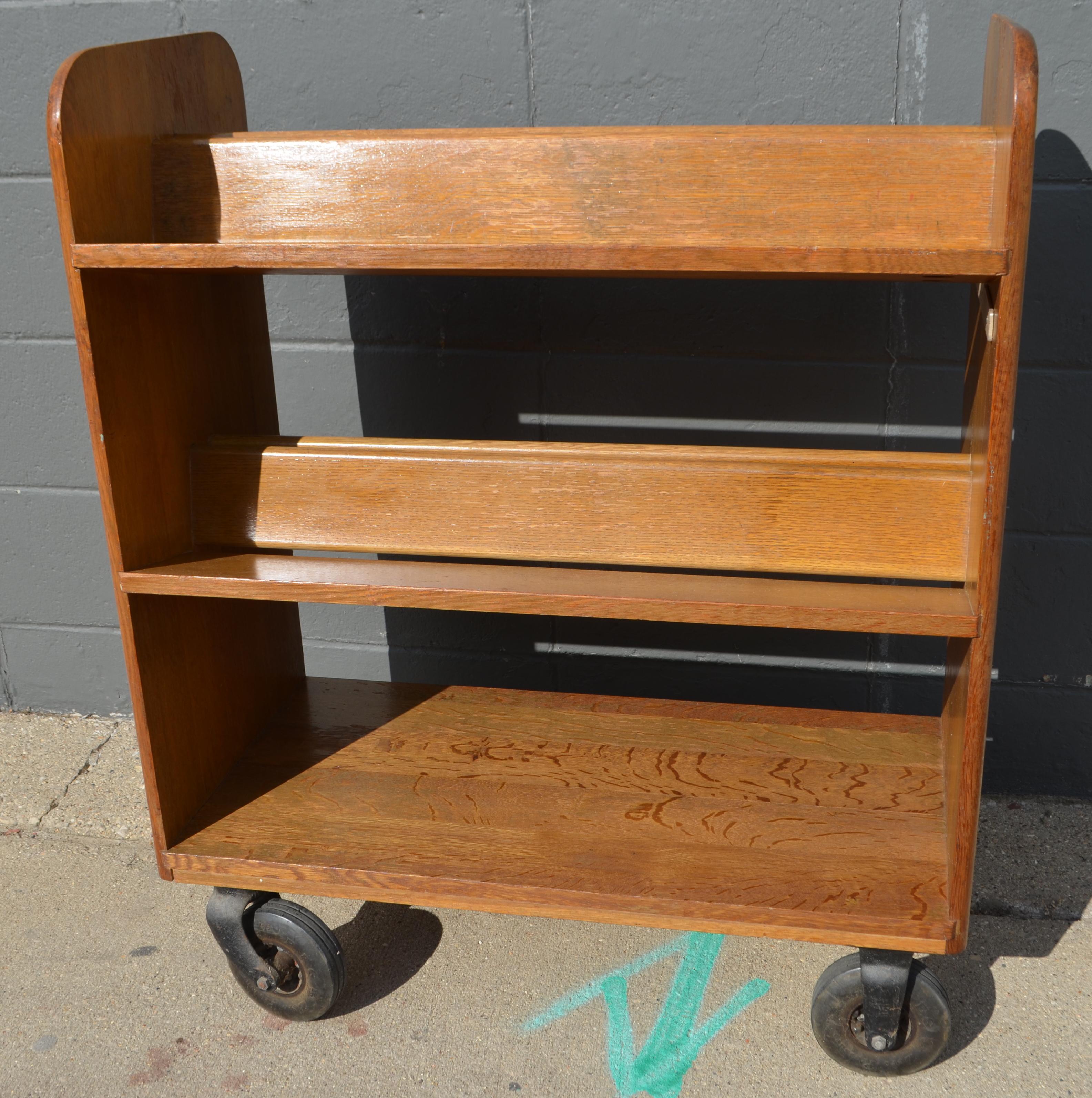 Midcentury oak book cart with slanted shelving on wheels from midwestern public library. Restored, cleaned and sealed. Top two shelves are slanted for stabile storage and transport of books, CDs and DVDs. Use it in the bathroom for accessories with