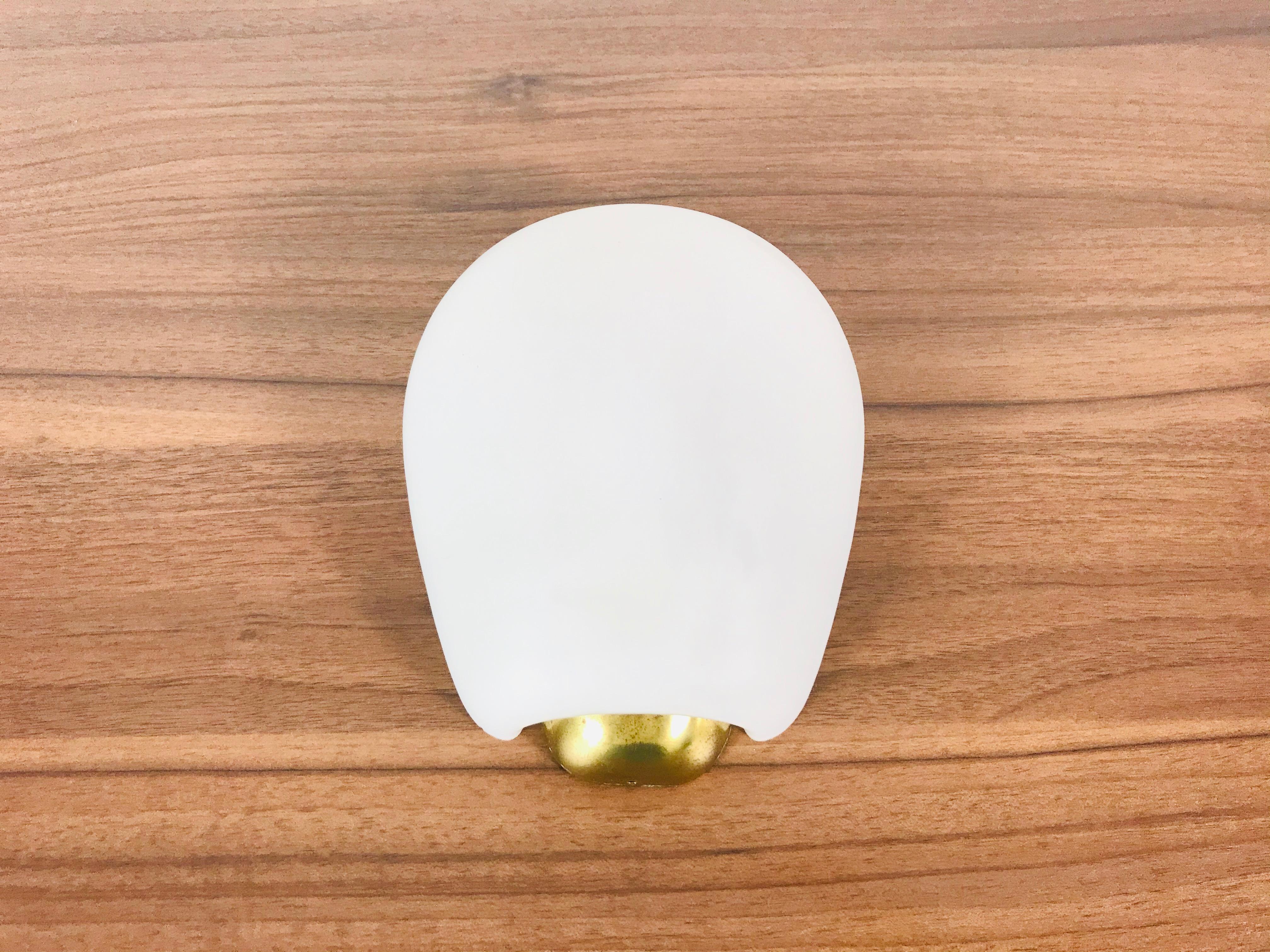 Beautiful midcentury wall lamp by Wilhelm Wagenfeld for Lindner. It was made in Germany in the 1960s. The opaline glass shade has an asymmetrical shape. The bottom part is made of brass.

The light requires one light bulb.