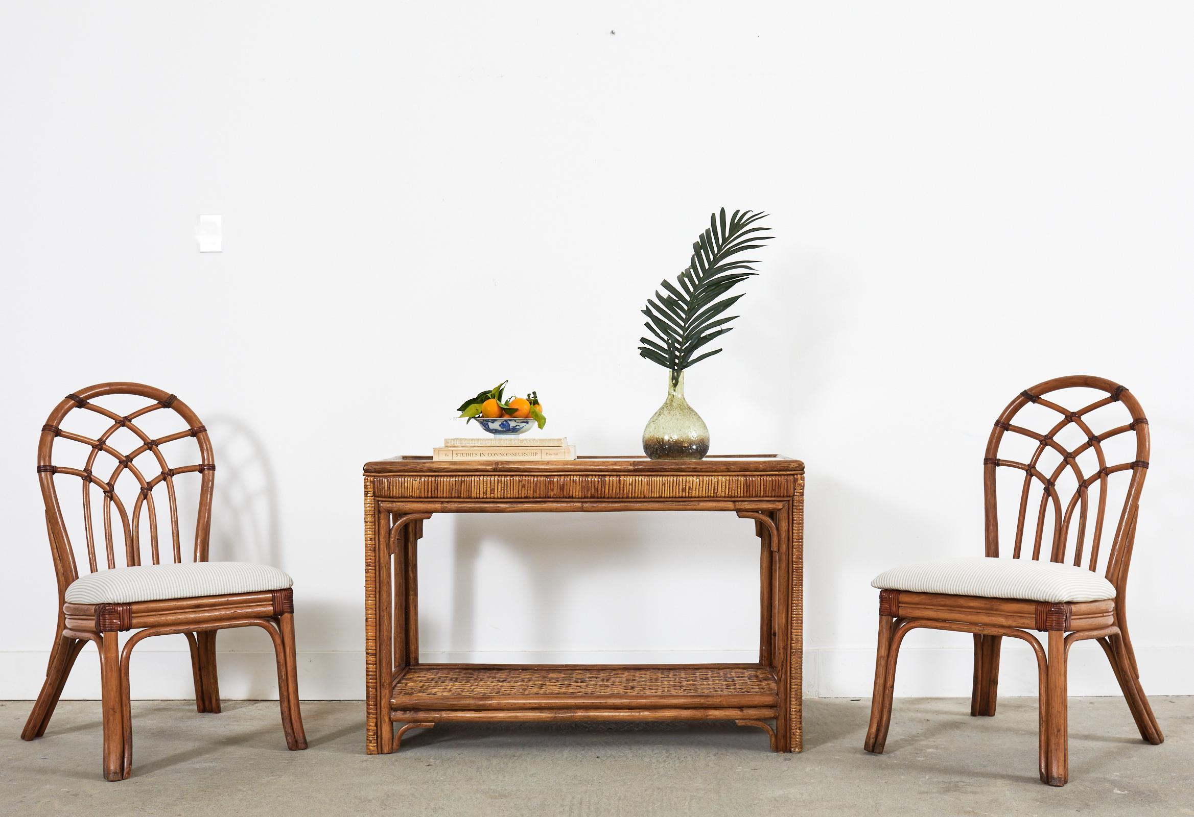 Handsome mid-century organic modern two-tier console table or sofa table. The console features a rattan frame with decorative bamboo veneered sides and legs. The bottom shelf has a woven rattan inset and the top has a geometric open fretwork design