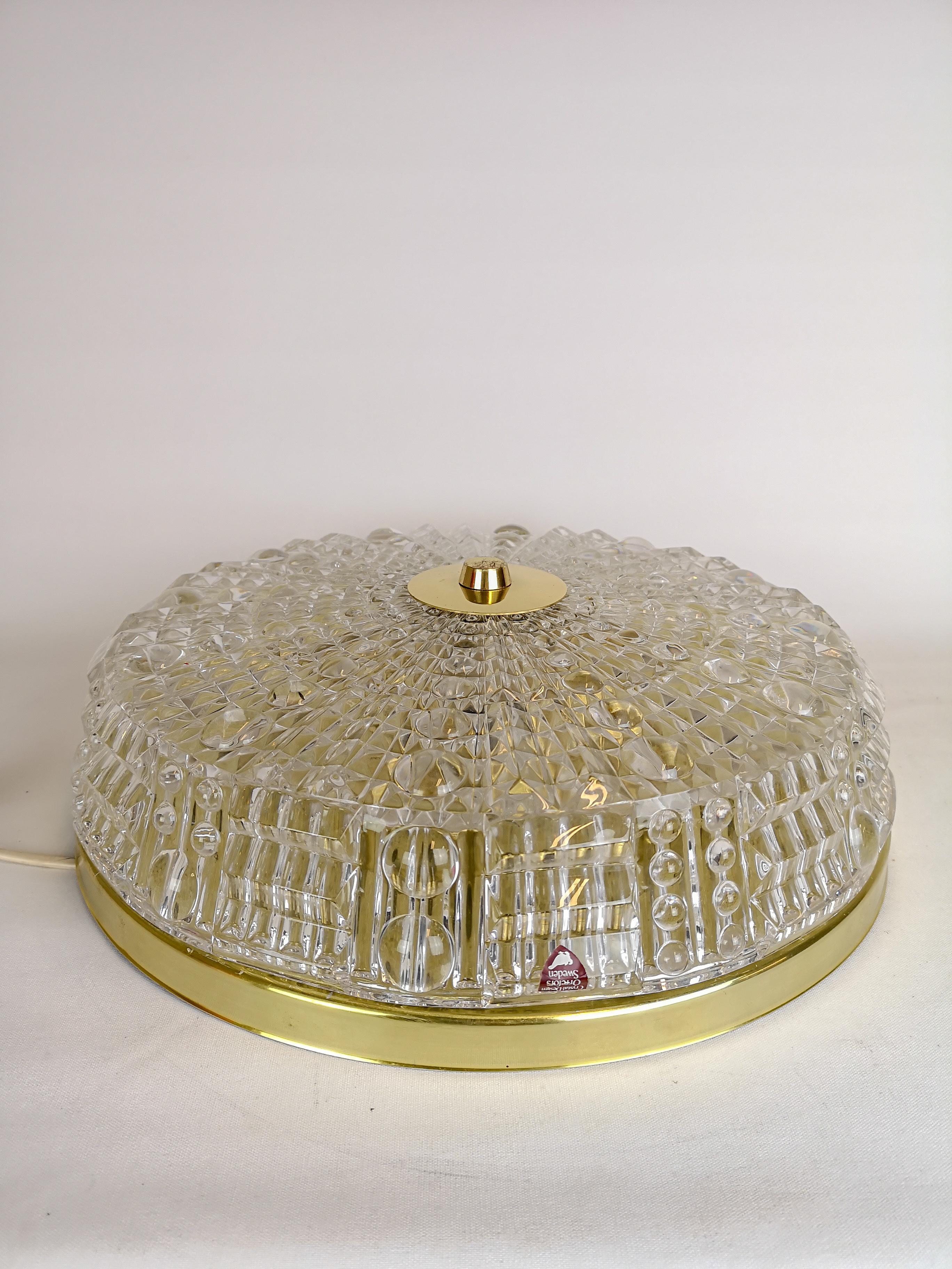 Midcentury crystal glass and brass ceiling light fixture, circa mid-1970s. Made at Orrefors and Designed by Carl Fagerlund. This lovely example is pressed clear crystal glass with brass accents. 

Good working condition. 

Measures: D 40 cm, H