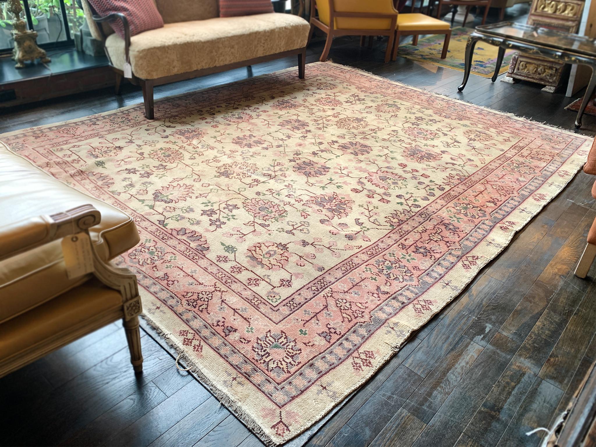Dieser in der Mitte des 20. Jahrhunderts handgeknüpfte Oushak-Teppich hat eine weiche, erdige Farbpalette aus Rosa und blassem Gelb mit Schattierungen von Blau, Grün und Rot. Das Design besteht aus einem zentralen Feld mit großen floralen