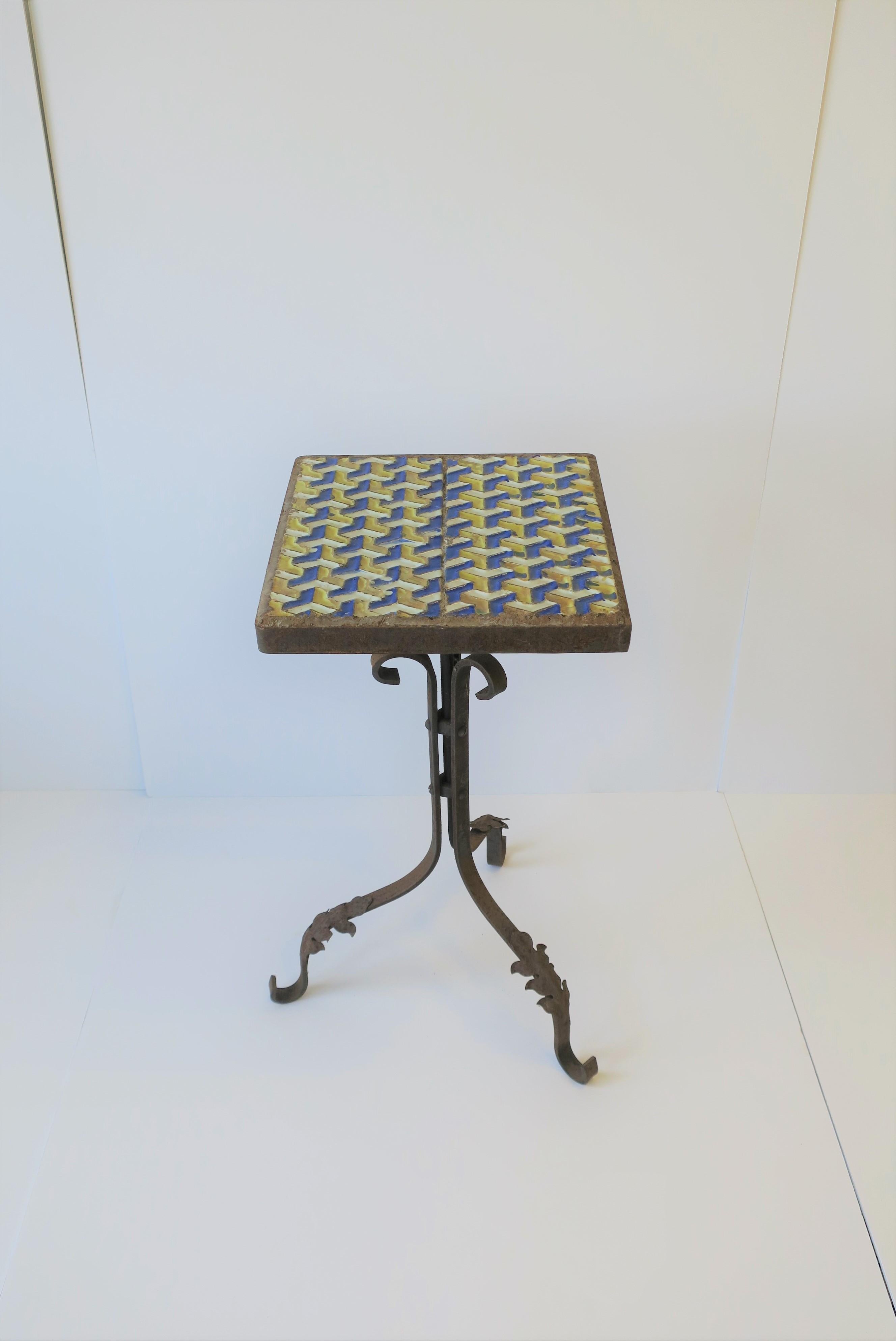 A substantial mid-20th century outdoor patio side table with a square ceramic or enamel top and tri-pod base legs. Table is 'weathered' iron and a modern geometric design top with colors that include: white, blue, and yellow. 

Table measures: 24