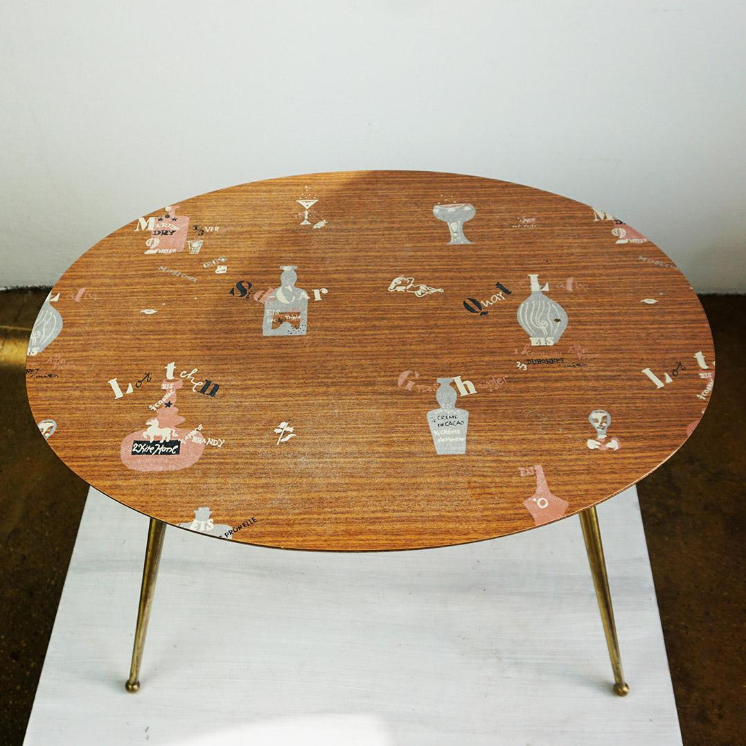 Questo charme del Midcentury  Il tavolino da caffè o da cocktail è stato prodotto in Germania intorno agli anni '50 da Ilse Möbel, come indicato sul lato inferiore. Presenta gambe in ottone e un piano ovale in laminato con un'incantevole barra e