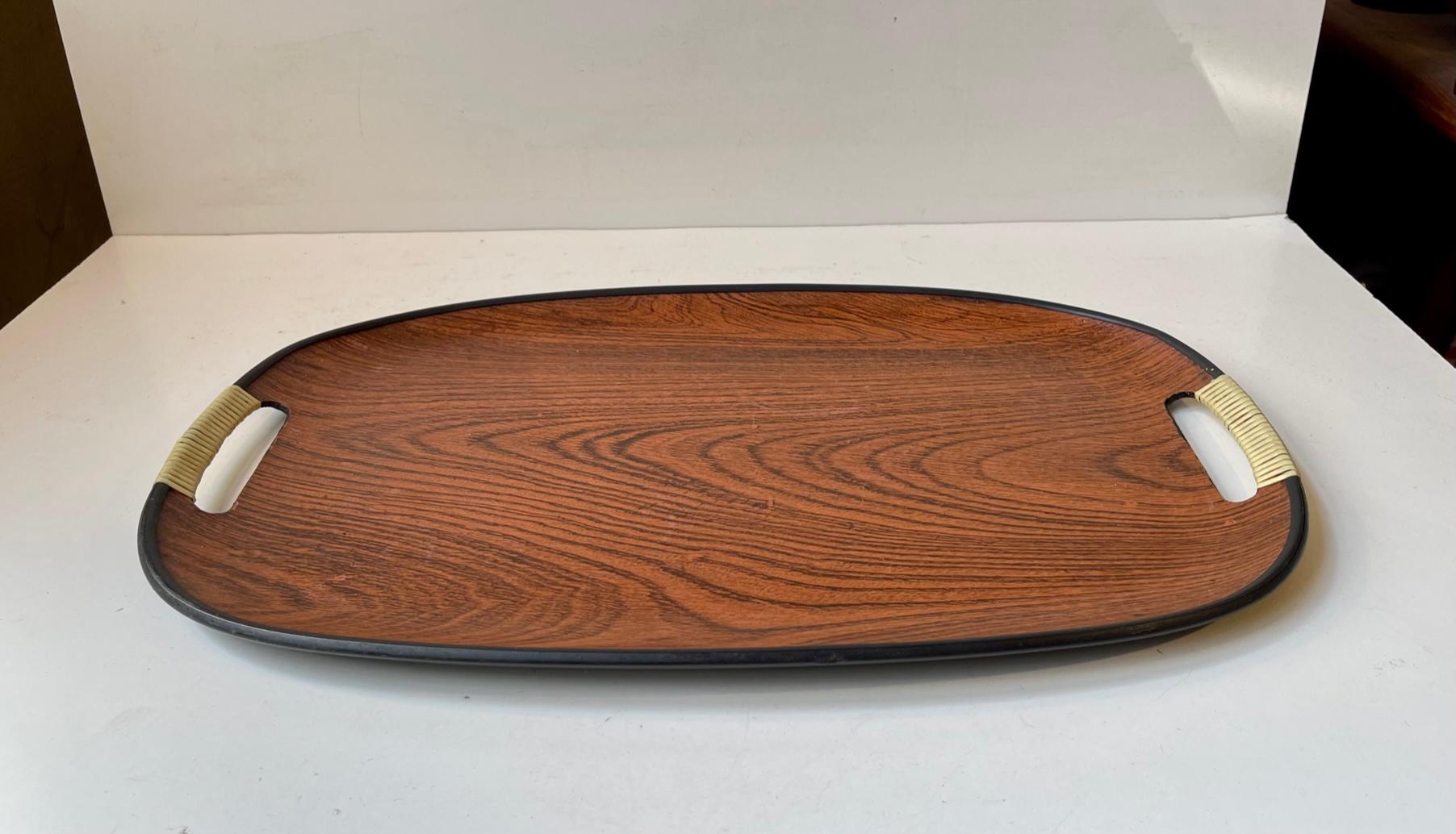 Midcentury ovale tray in faux wood (its made from formica with a plastic veneer imitating wood/oak. It features acrylic rattan to its integrated handles. Measurements: L: 45 cm, Dept: 29.5 cm, Height: 2 cm.