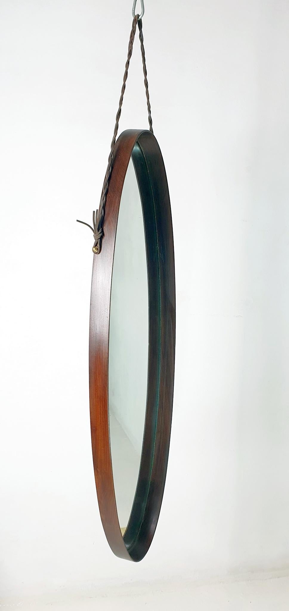 An oval mirror by Italian duo Campo e Graffi in teak wood hanging from a braided leather string. In nice sound condition in both glass and wood frame.