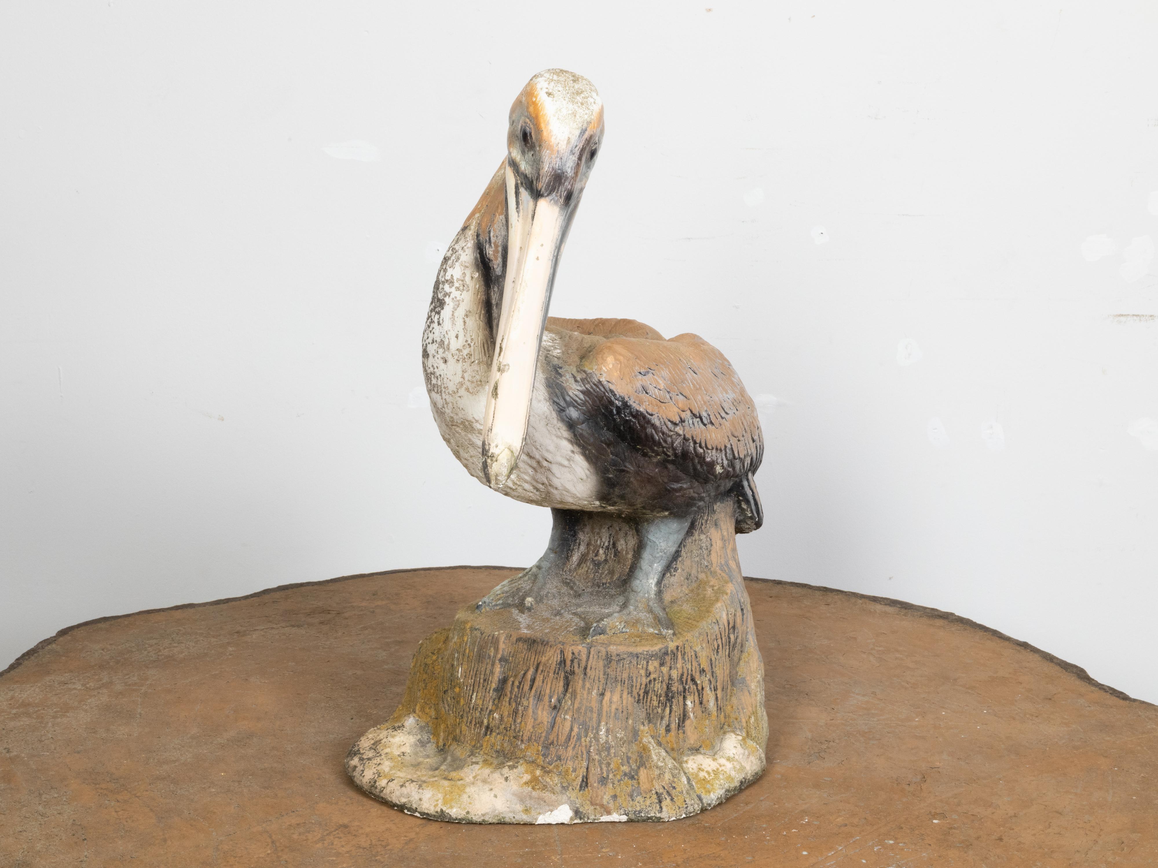 A painted concrete pelican sculpture from the mid 20th century, with nicely distressed patina. Created during the midcentury period, this statue captures our attention with its charming depiction of a pelican standing on a rocky formation. Adorned