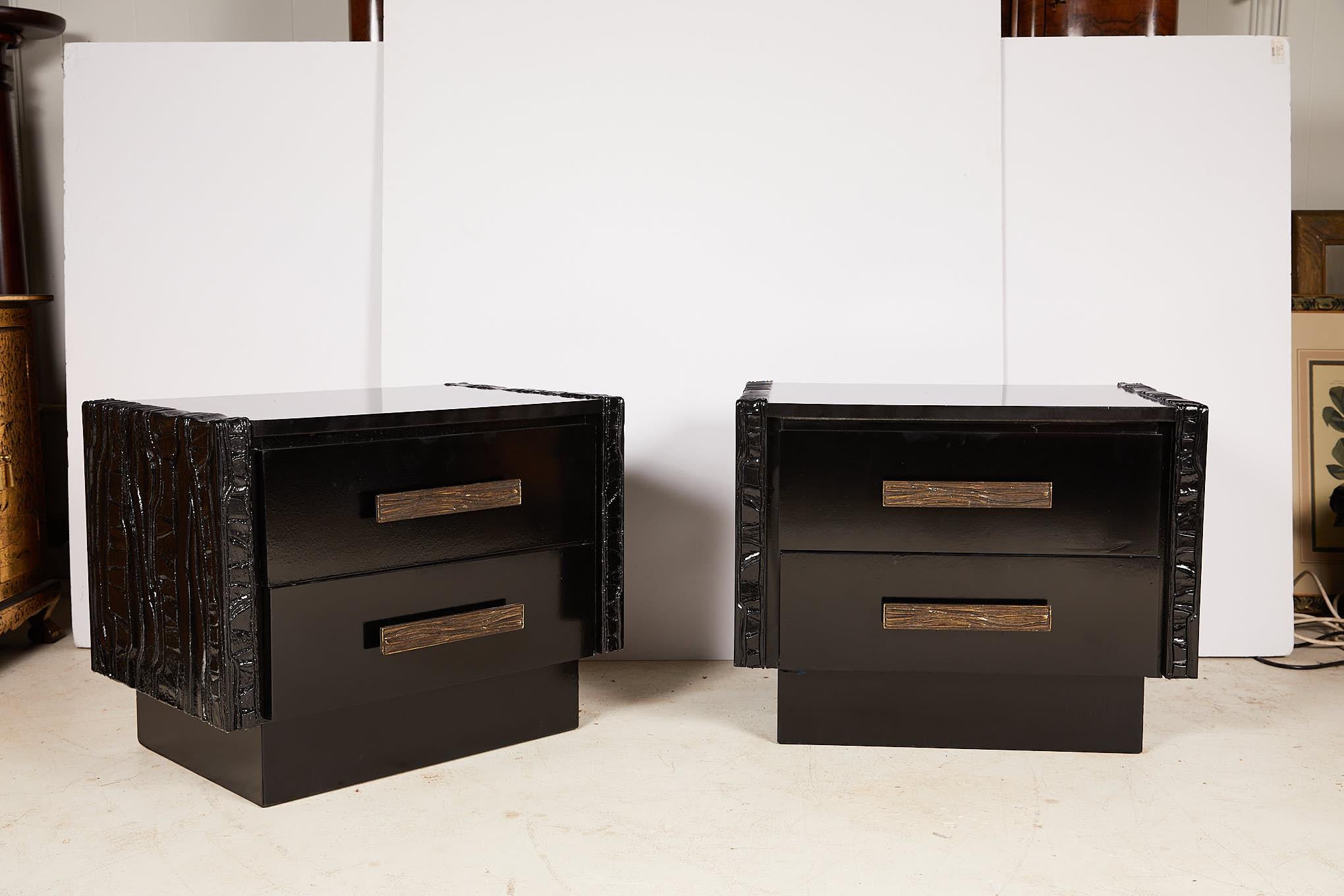 Vintage pair of midcentury nightstands or end tables with heavy brutalist carvings on each side flanking a case holding two drawers with heavy bronze cast hardware and raised on a plinth base. The tables are made of walnut and have a black lacquer