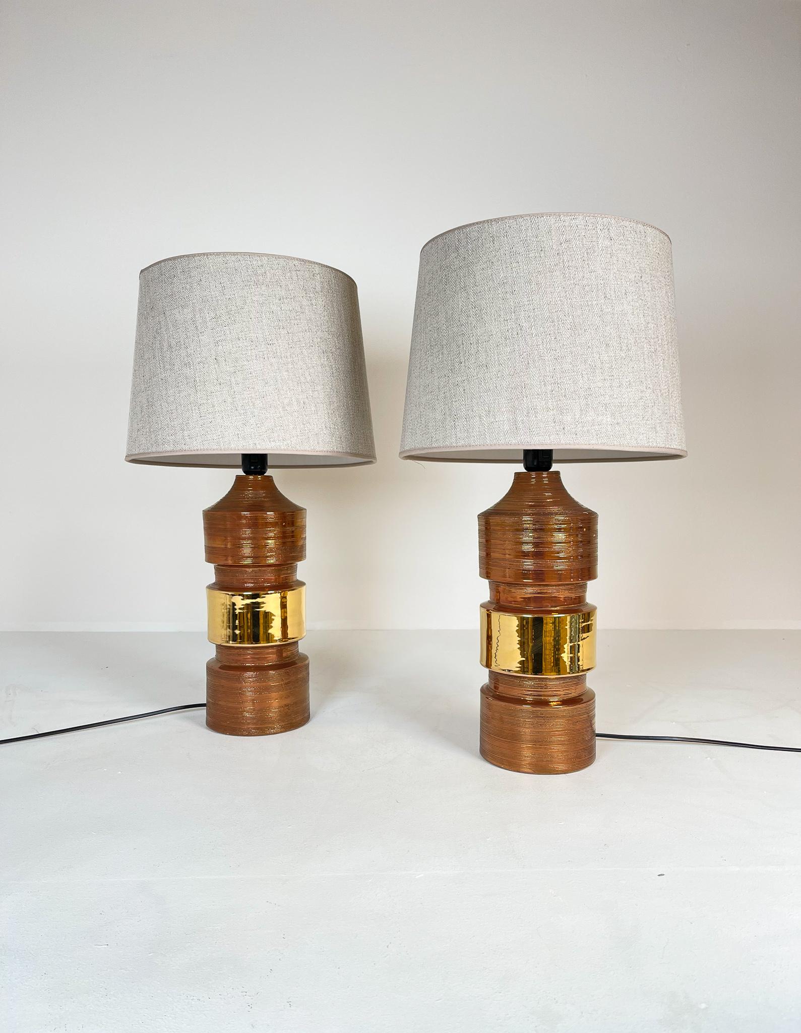 Large and heavy pair of cylinder-shaped table lamps made in ceramic with elegant matte copper glaze finish with a golden stripe. Bittosi design with all new shades, made in Sweden. This pair of table lamps will give that great look to a vintage home