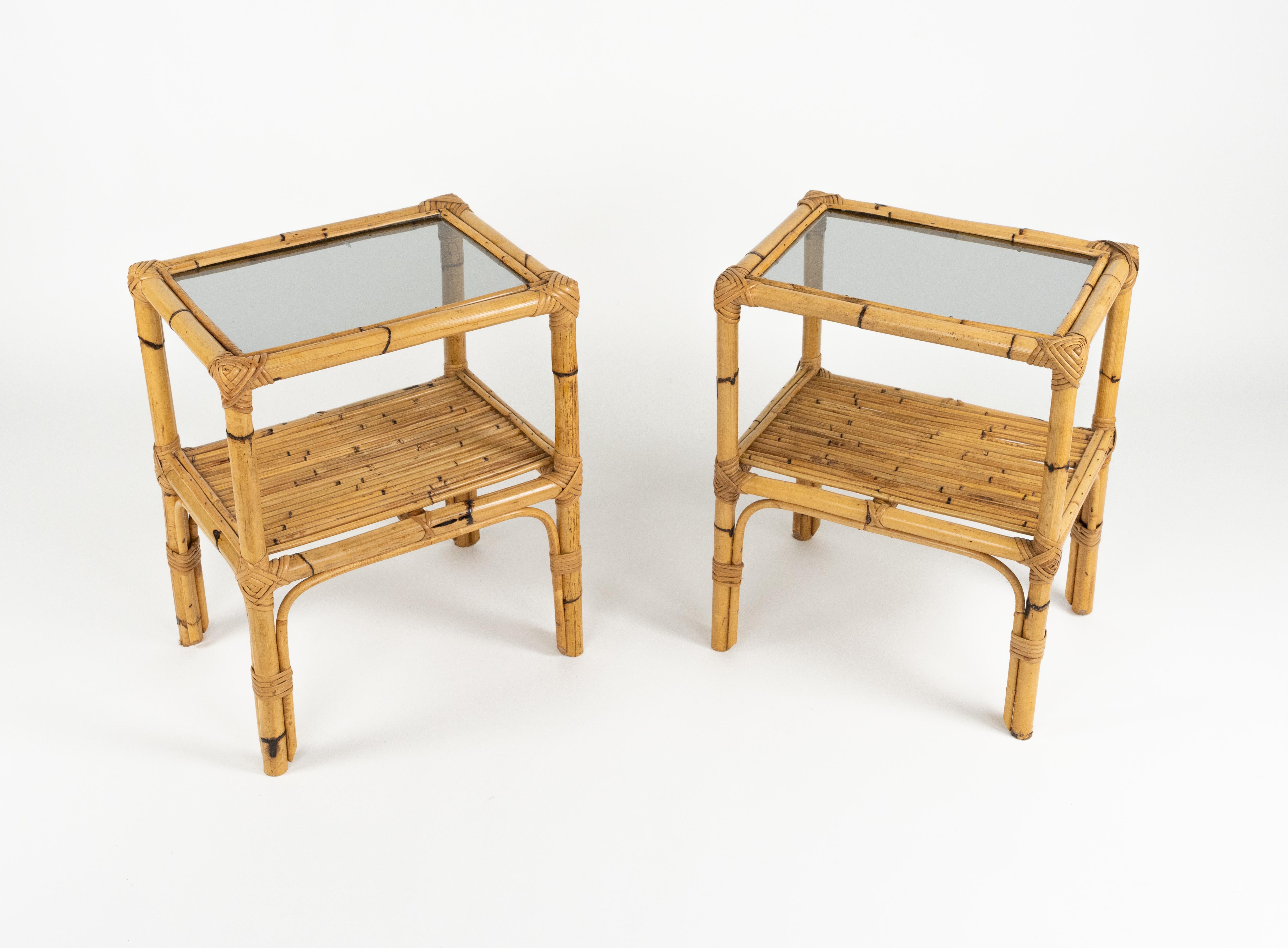 Coppia di tavolini o comodini a due livelli in bambù, rattan e vetro.  

Prodotto in Italia negli anni '1960.