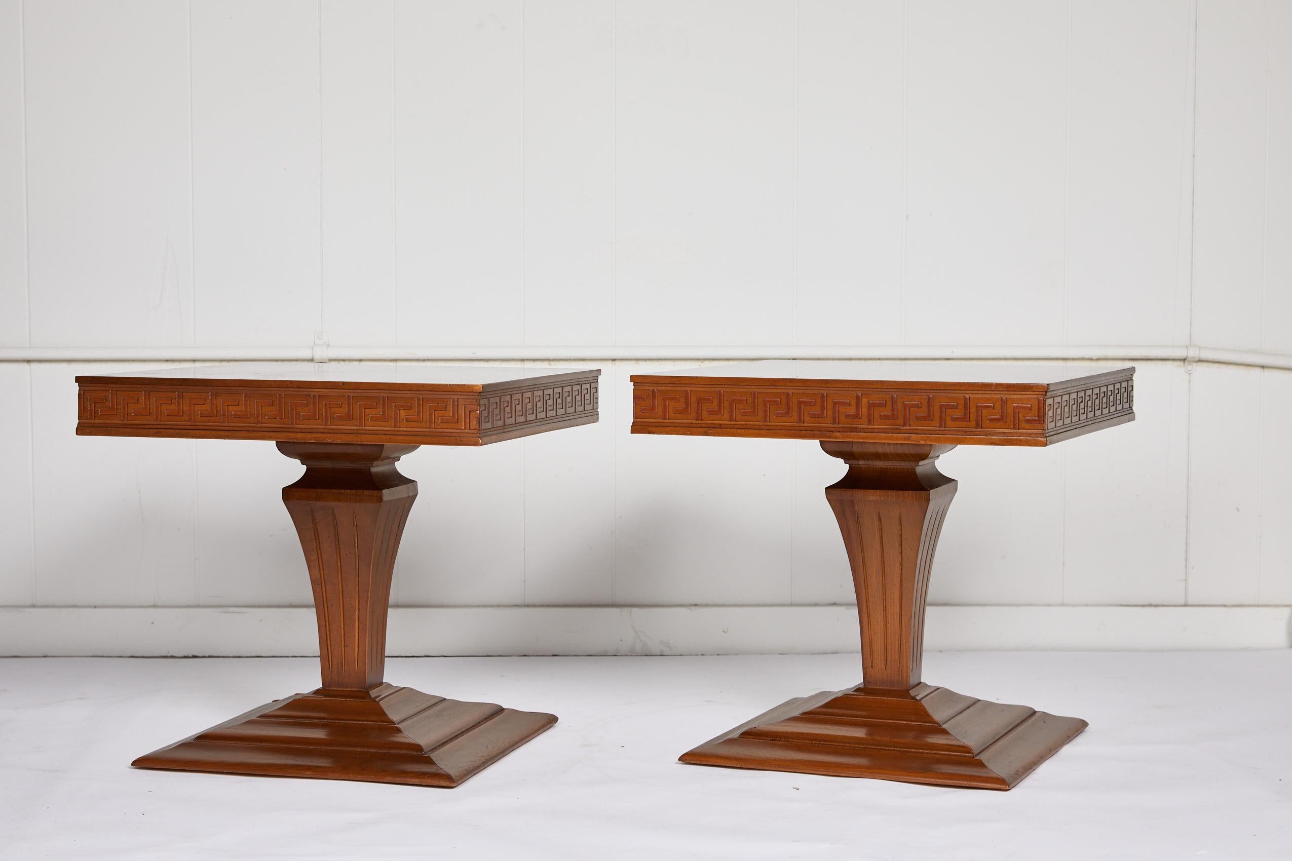 Midcentury pair of low square side or end tables with a checkered veneer top and Greek key apron over a carved urn shaped pedestal and tiered platform base. The vintage tables are symmetrical and finished on all sides.