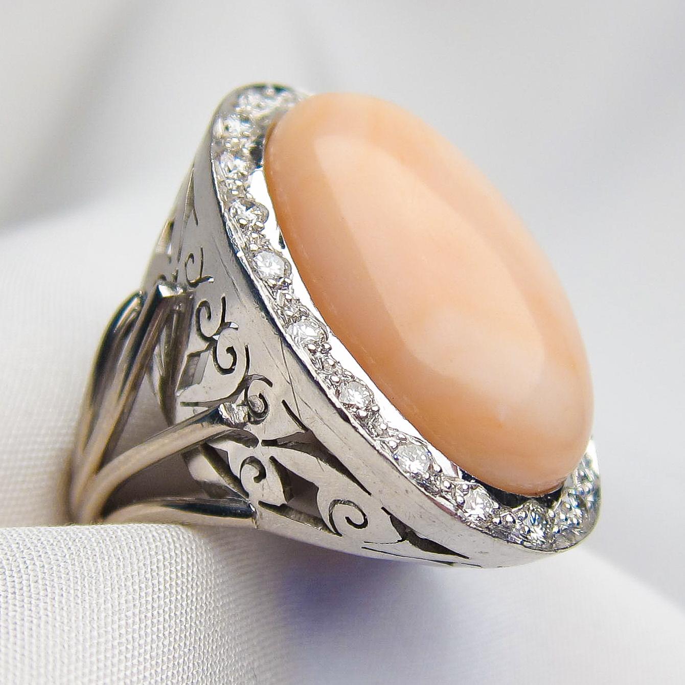 This magnificent midcentury halo ring features an amazing 17.3 carat, oval cabochon-cut pink coral. Bead-set around the coral are 20 round, brilliant-cut diamonds weighing a total of .60 carats, with a VS2 clarity and G-H color. The palladium scroll