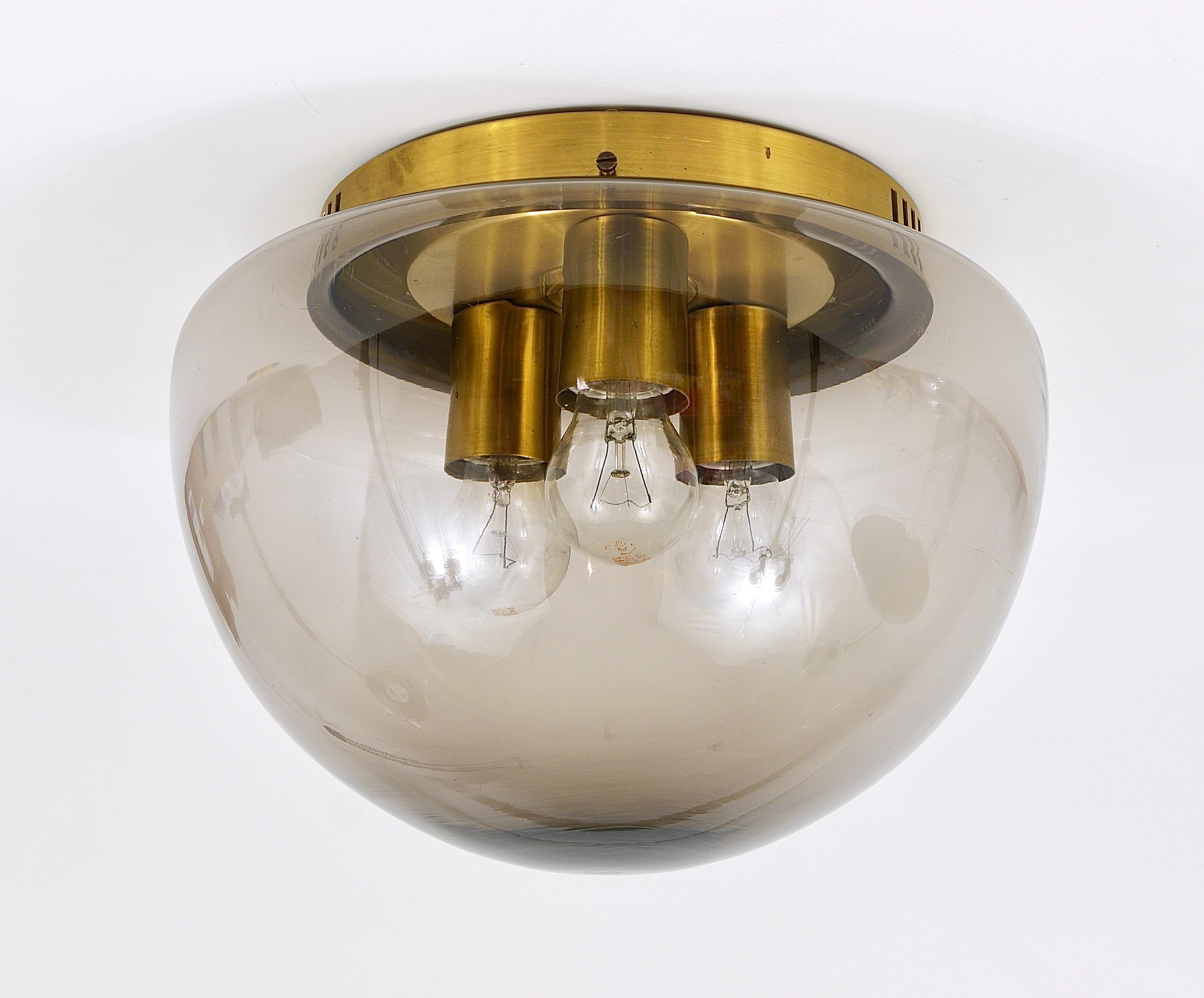 A beautiful brass flushmount from the 1970s. With a globe lampshade, made of smoked grey glass. Executed by Peill & Putzler / Germany in the 1970s. Has three light sources and is in good condition with marginal wear.