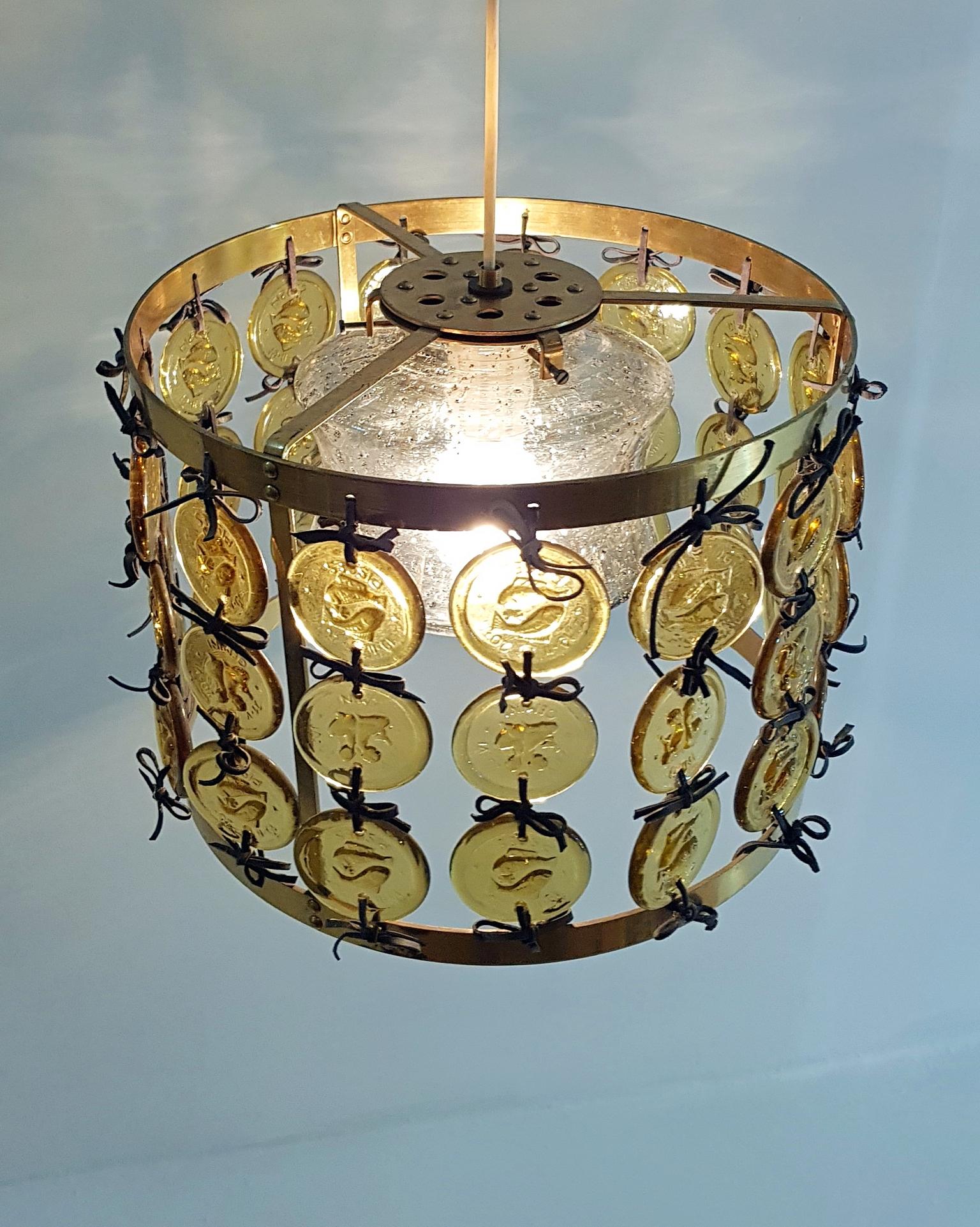 Rare celling lamp by Swedish designer Erik Höglund for glass maker Kosta Boda Glass manufacturers. The frame is made in brass with attached round pieces of glass depicting the star signs Pisces and Gemini bound together in black leather strings. In