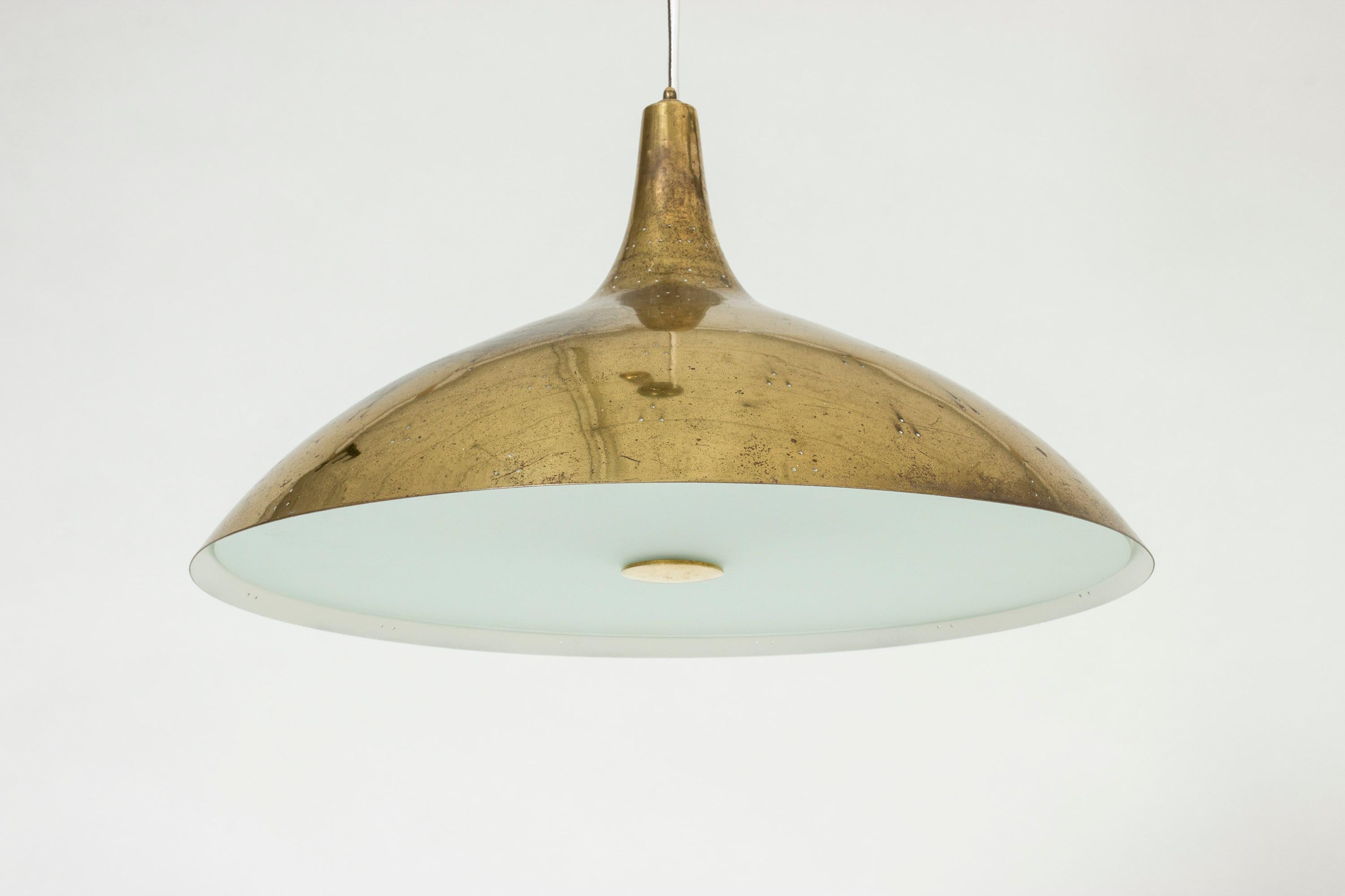 Elegant brass ceiling lamp by Paavo Tynell, with a streamlined shade perforated with small holes. The underside of the lamp has a glass shade that covers the light source. Suspended with a brass cord, height adjustable with a brass