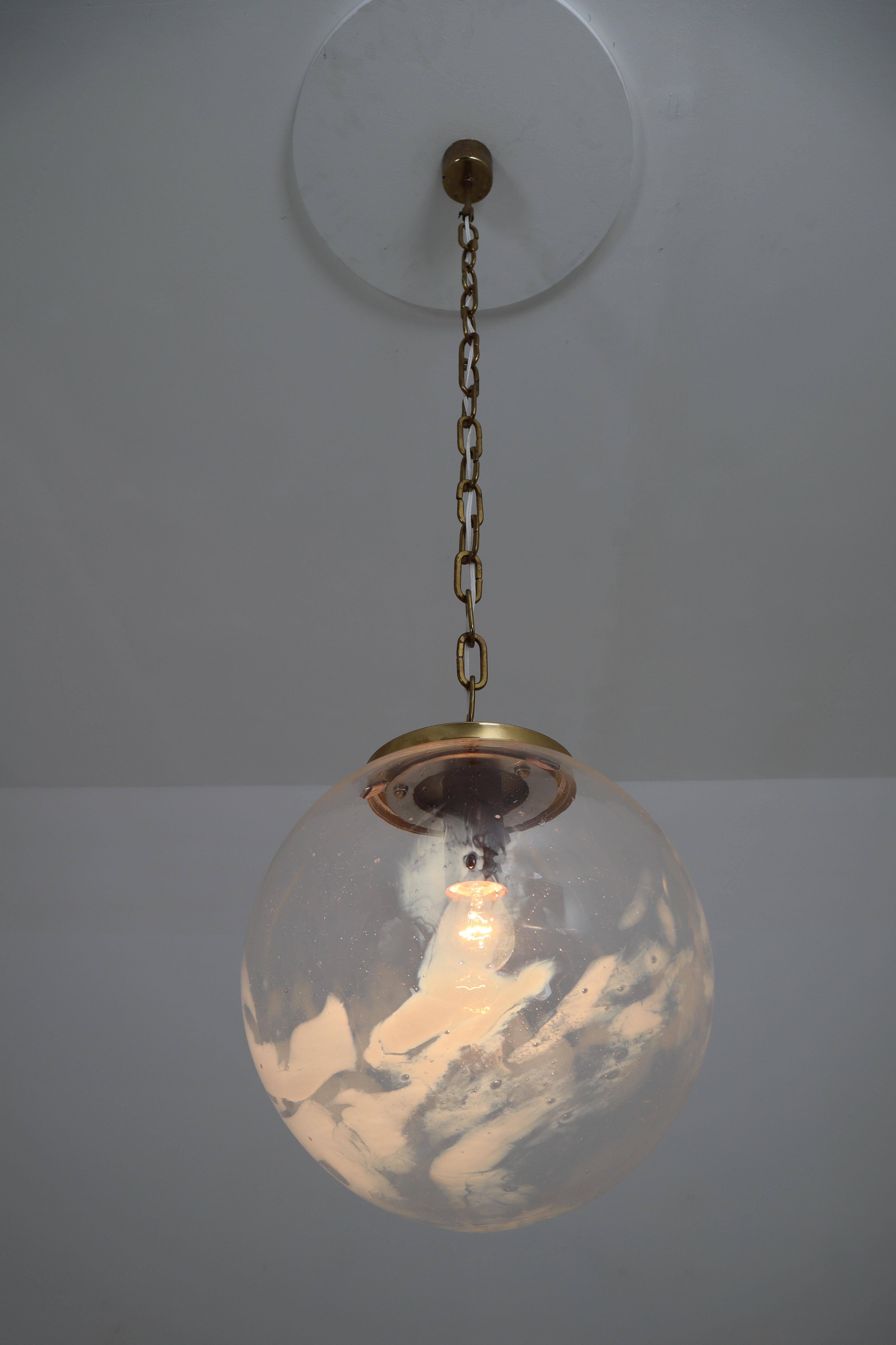 Two midcentury pendants, in brass and glass, European, 1970s.

Large ceiling lamp-pendants with brass and large handblown art-glass globe. These clear handblown glass globe are decorated with white streaks. The globe show a different and unique