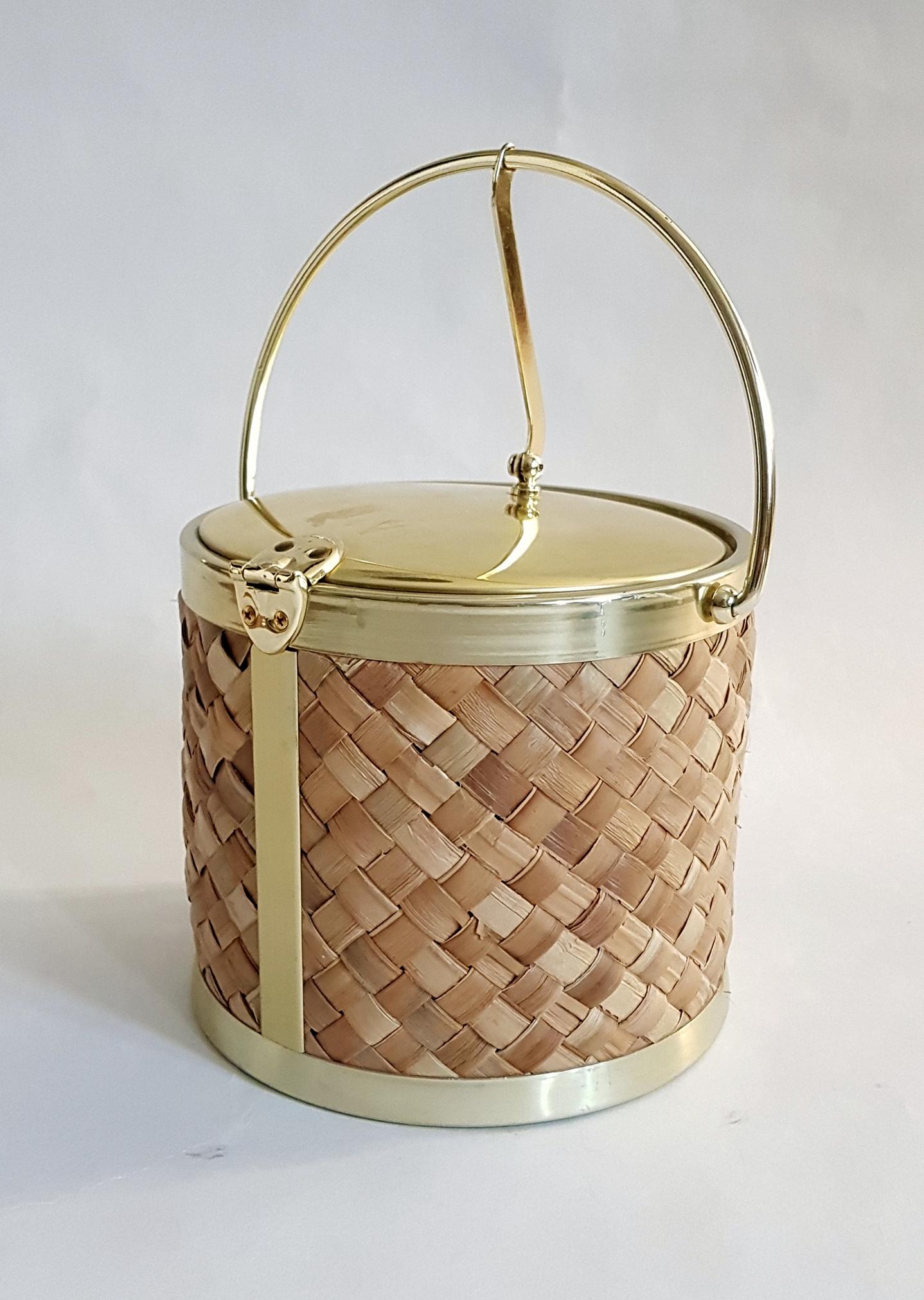 Super trendy and functional ice bucket by Kraftware Co. New York. Made in gold and raffia with the inside bucket in plastic with the inside of the lid is enameled in white.
The lid opens once you push down the handle and doesn’t have to be removed