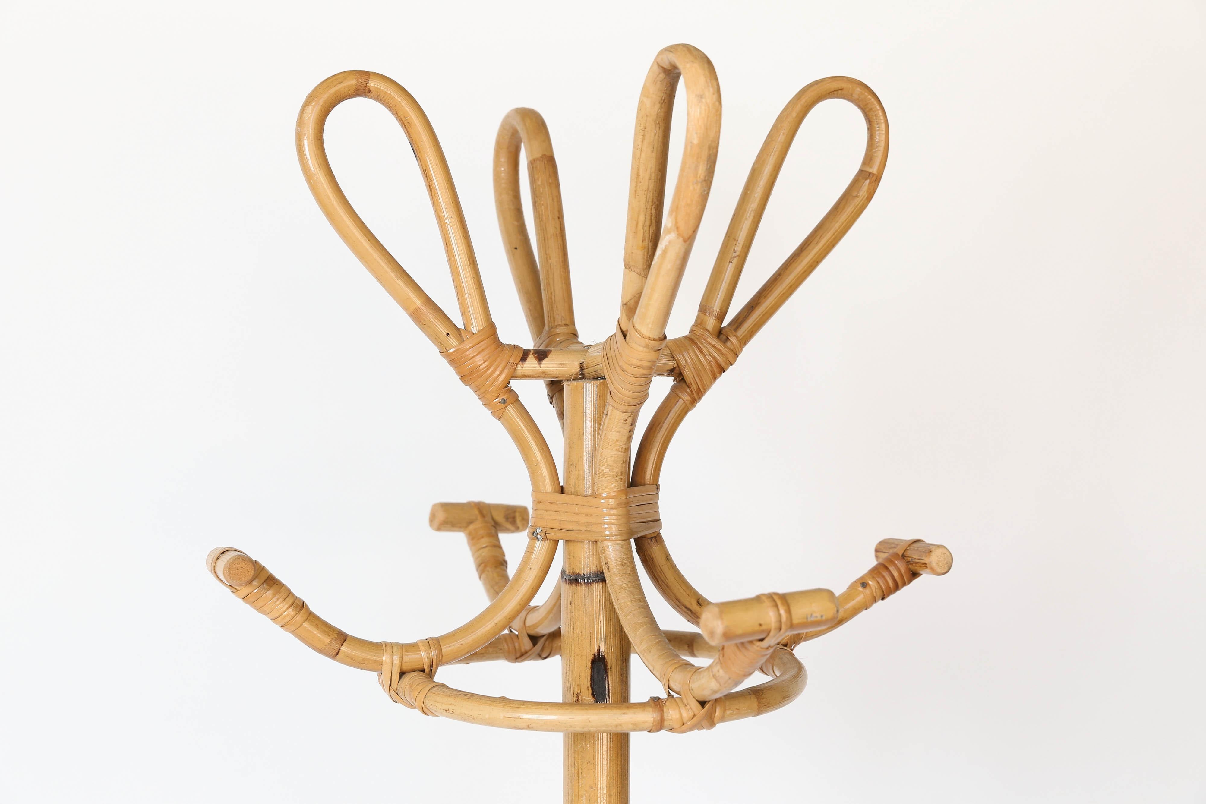 Midcentury coat and hat stand made of rattan. A decorative item as well as useful. With four hooks to hang hats and four hooks for coats, the piece stands on the floor with four legs and a decorative ring around the base.