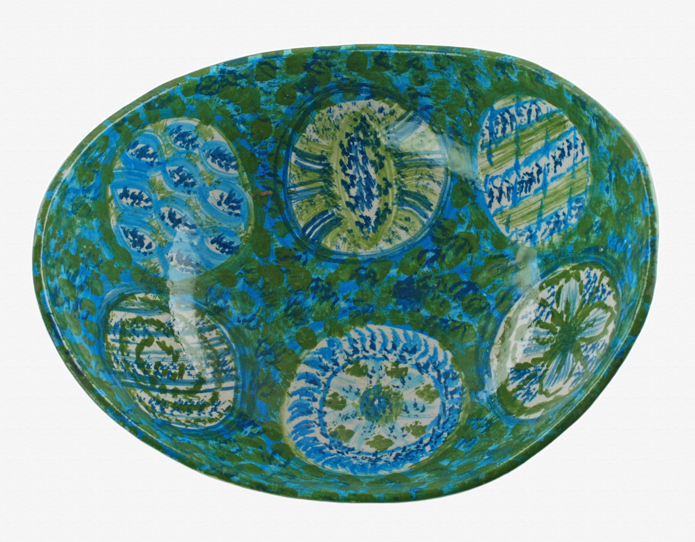 Este inusual cuenco de centro de mesa de cerámica se fabricó en Italia para el importador estadounidense Raymor. La pieza tiene forma de cuchara alargada y ha sido pintada a mano en tonos azules y verdes. El interior esponjado presenta seis formas